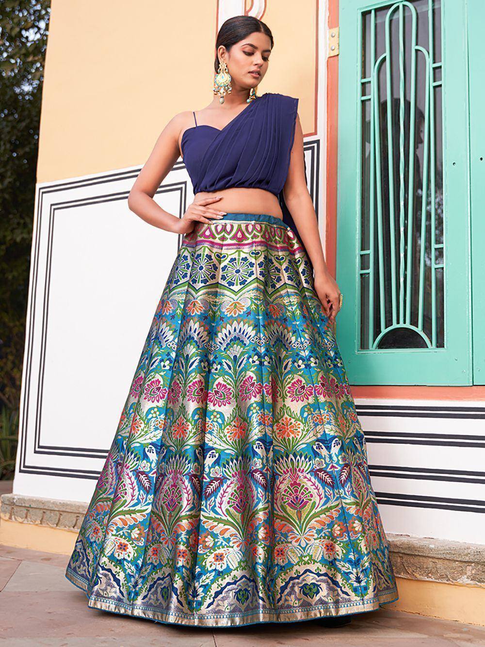 Woman in blue one-shoulder top with colorful floral lehenga skirt, ethnic Indian wear