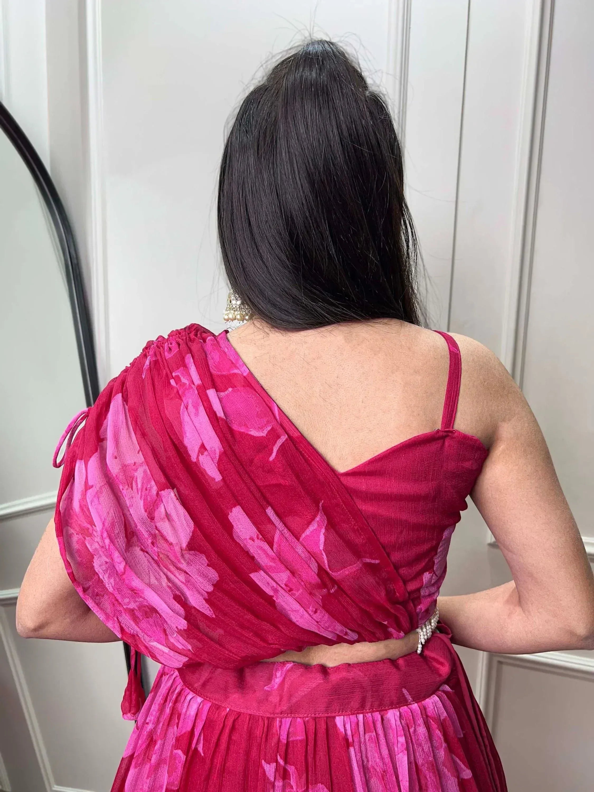 Back view of woman in pink floral ethnic gown with draped sleeves and pearl belt, showcasing designer Indian wear.