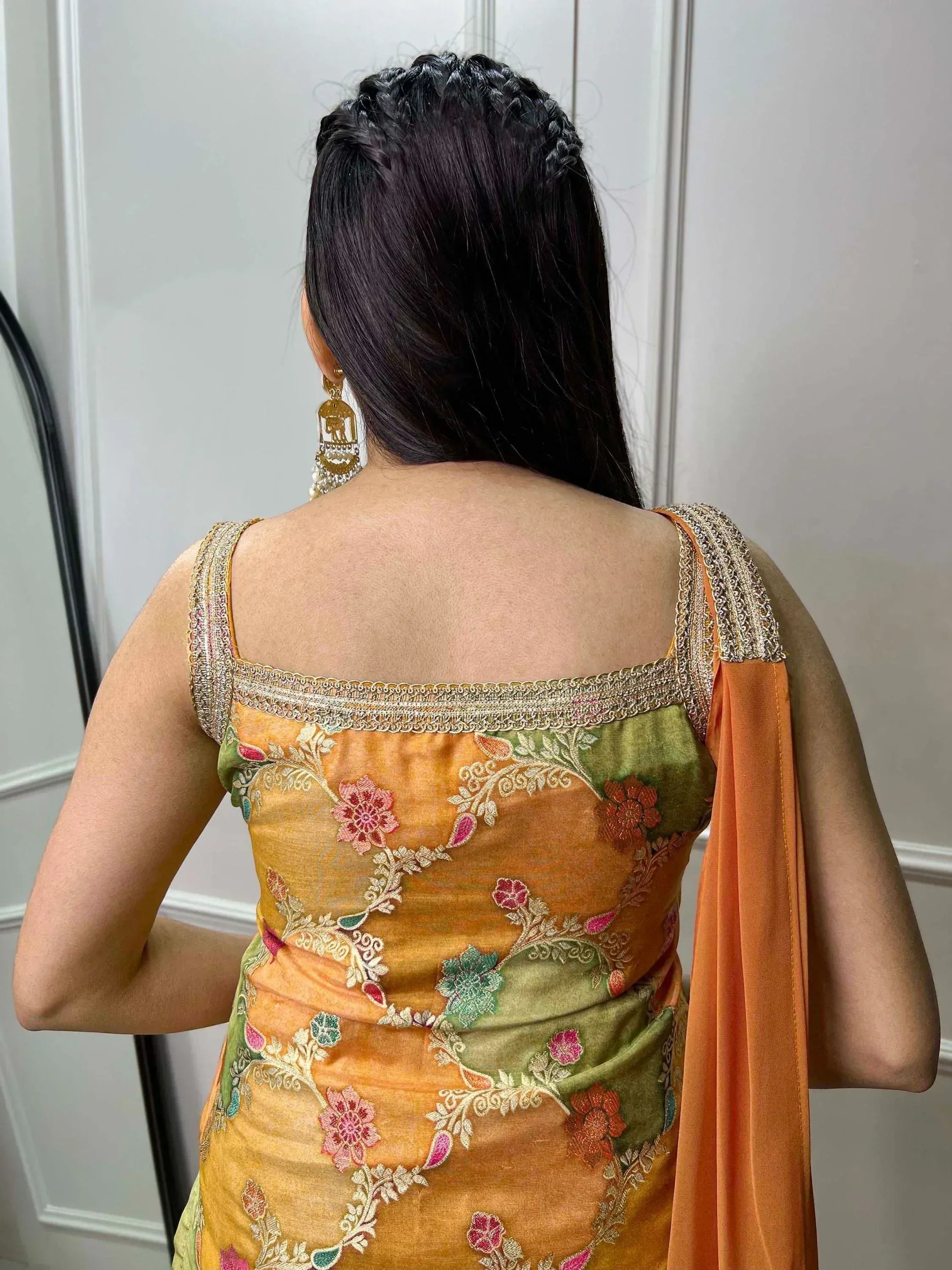 Back view of woman in embroidered orange and green Indian ethnic gown with floral design and gold trim