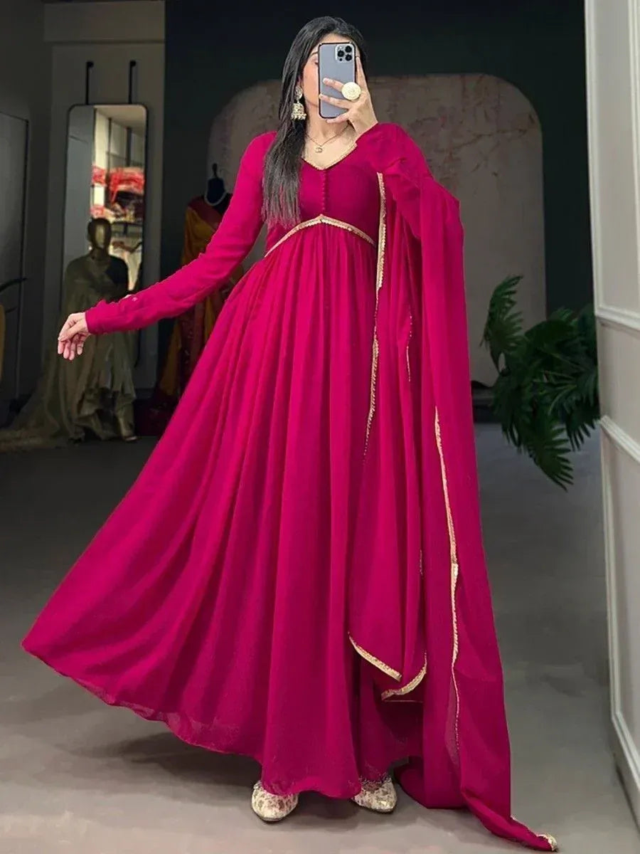 Vibrant pink ethnic gown with gold trim, long sleeves, and flowing cape, perfect for Indian festive occasions.