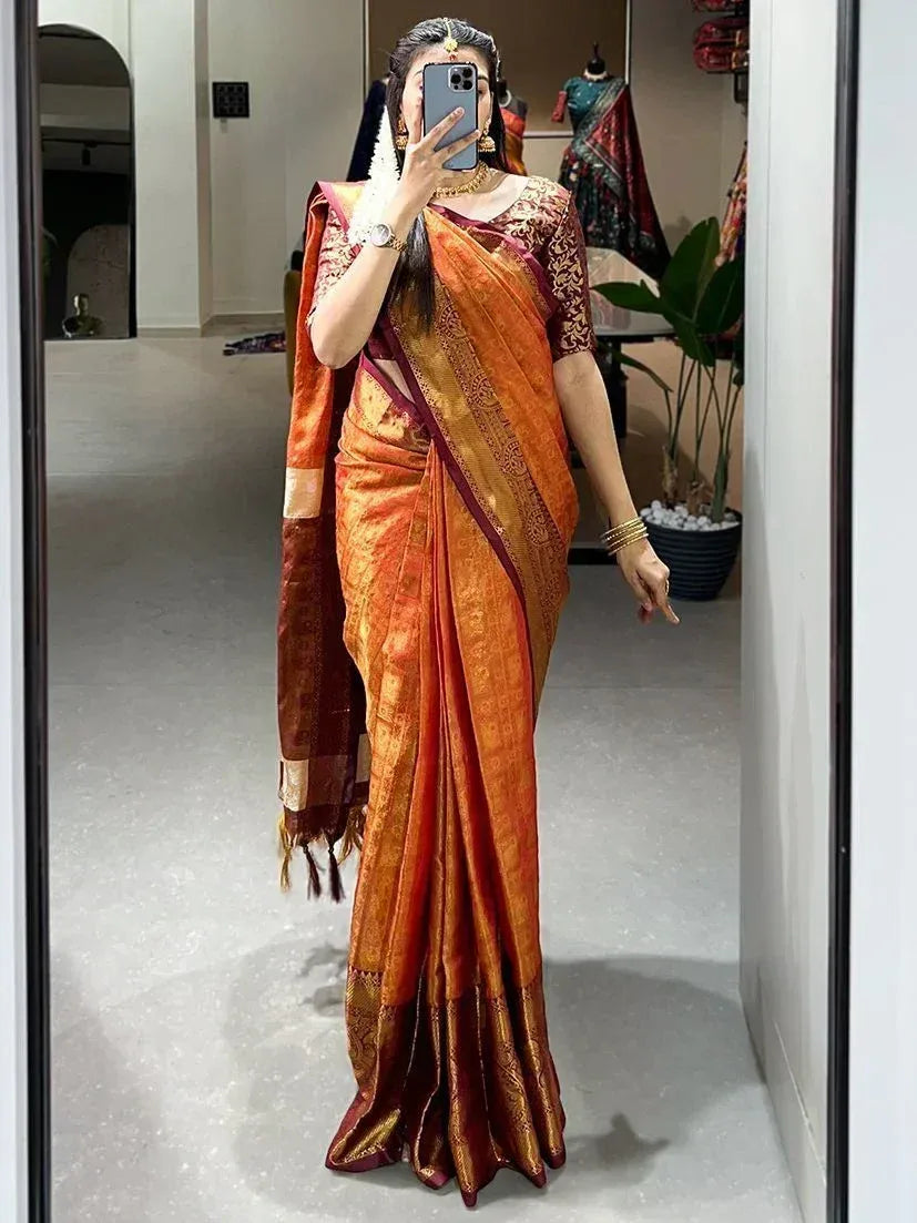Woman in orange and maroon silk saree with gold embroidery, taking mirror selfie in boutique