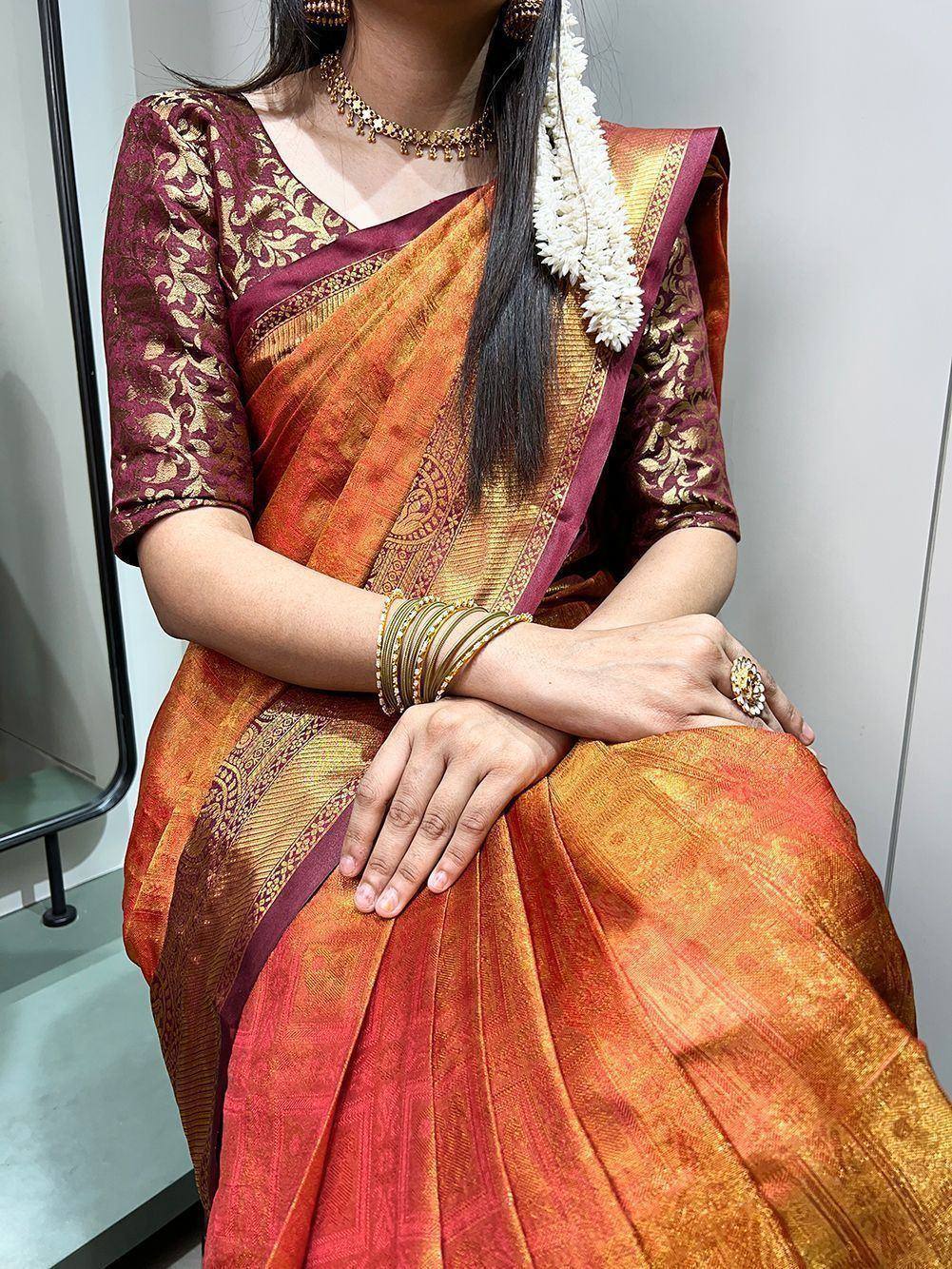 Orange and maroon designer saree with gold embroidery, paired with matching blouse and floral hair accessory