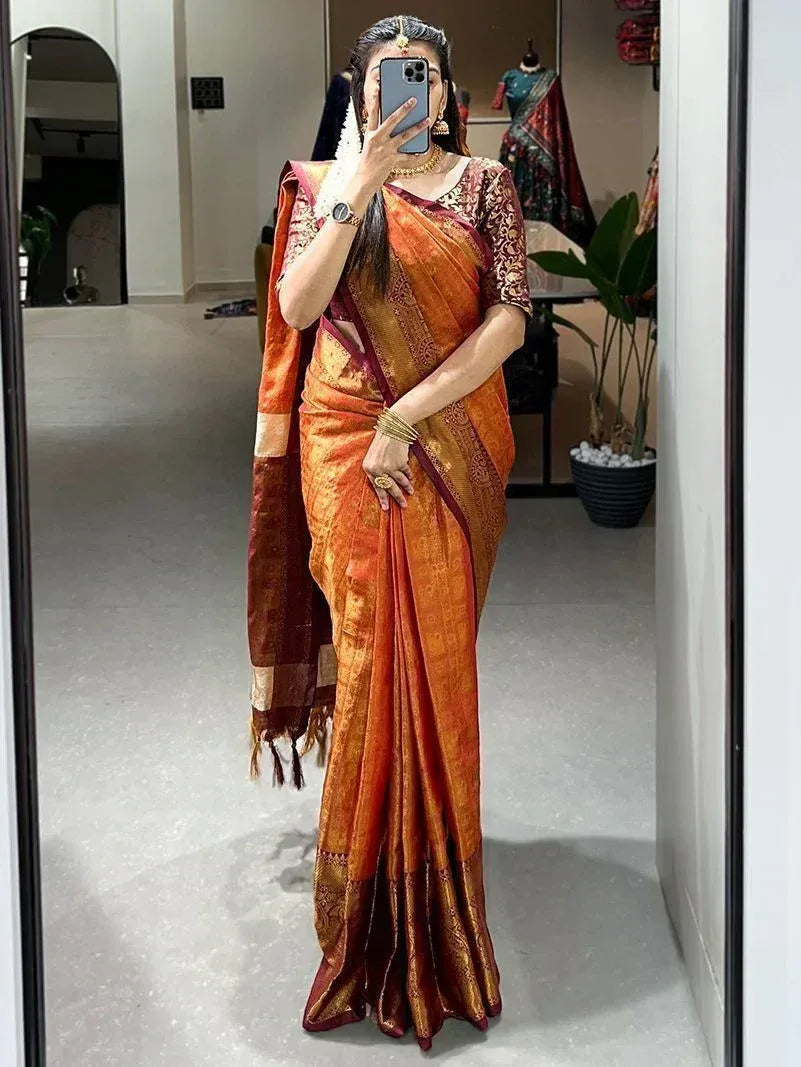 Woman wearing orange and maroon designer saree with gold embroidery, taking mirror selfie in boutique