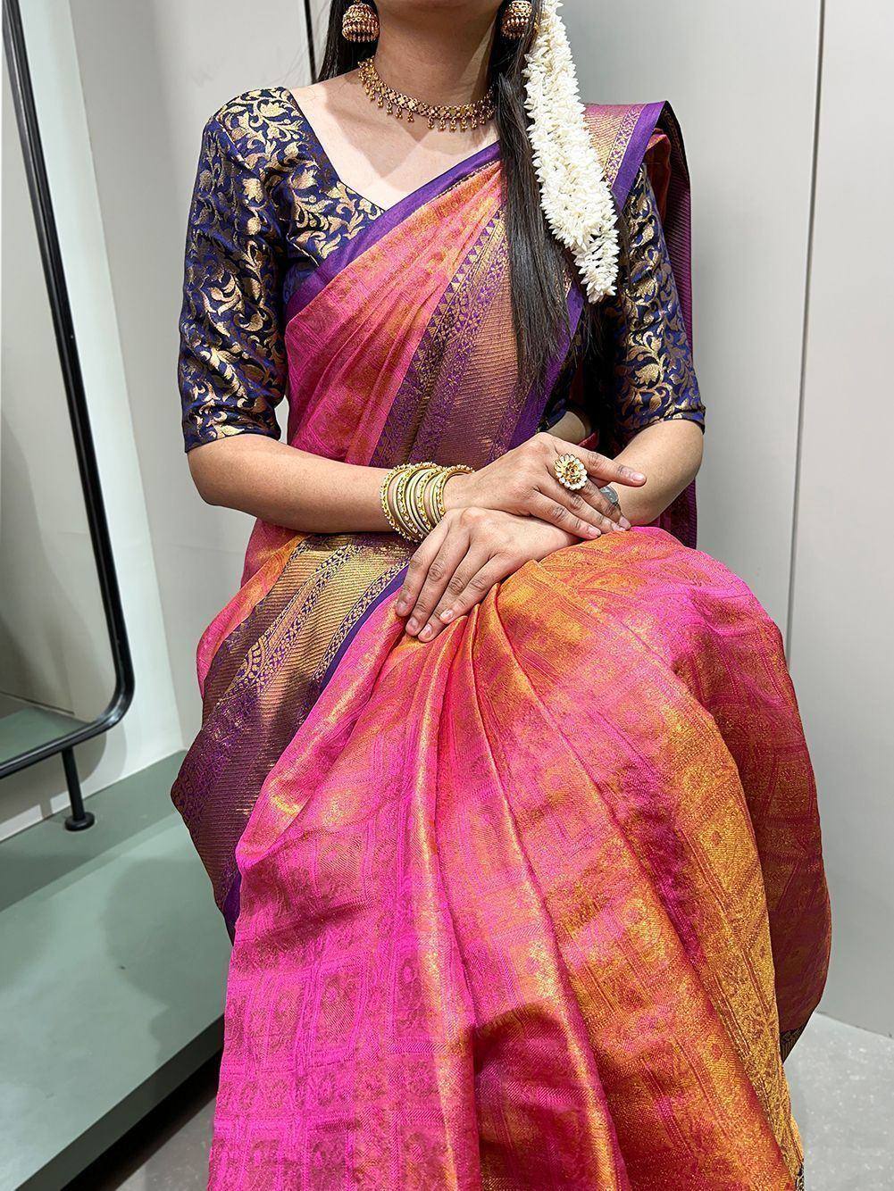 Vibrant pink and gold silk saree with purple blouse, traditional Indian ethnic wear, adorned with gold jewelry and floral garland