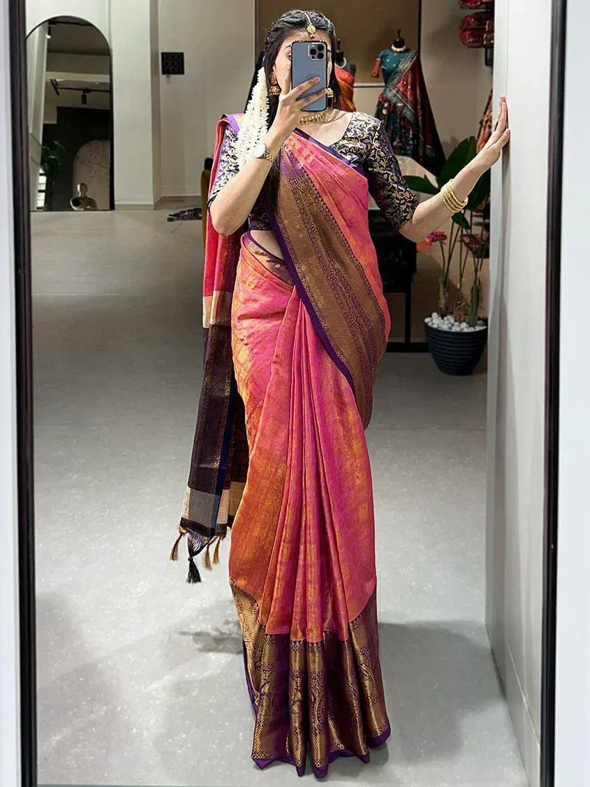 Woman in pink and gold designer saree with purple border, taking mirror selfie in ethnic wear store
