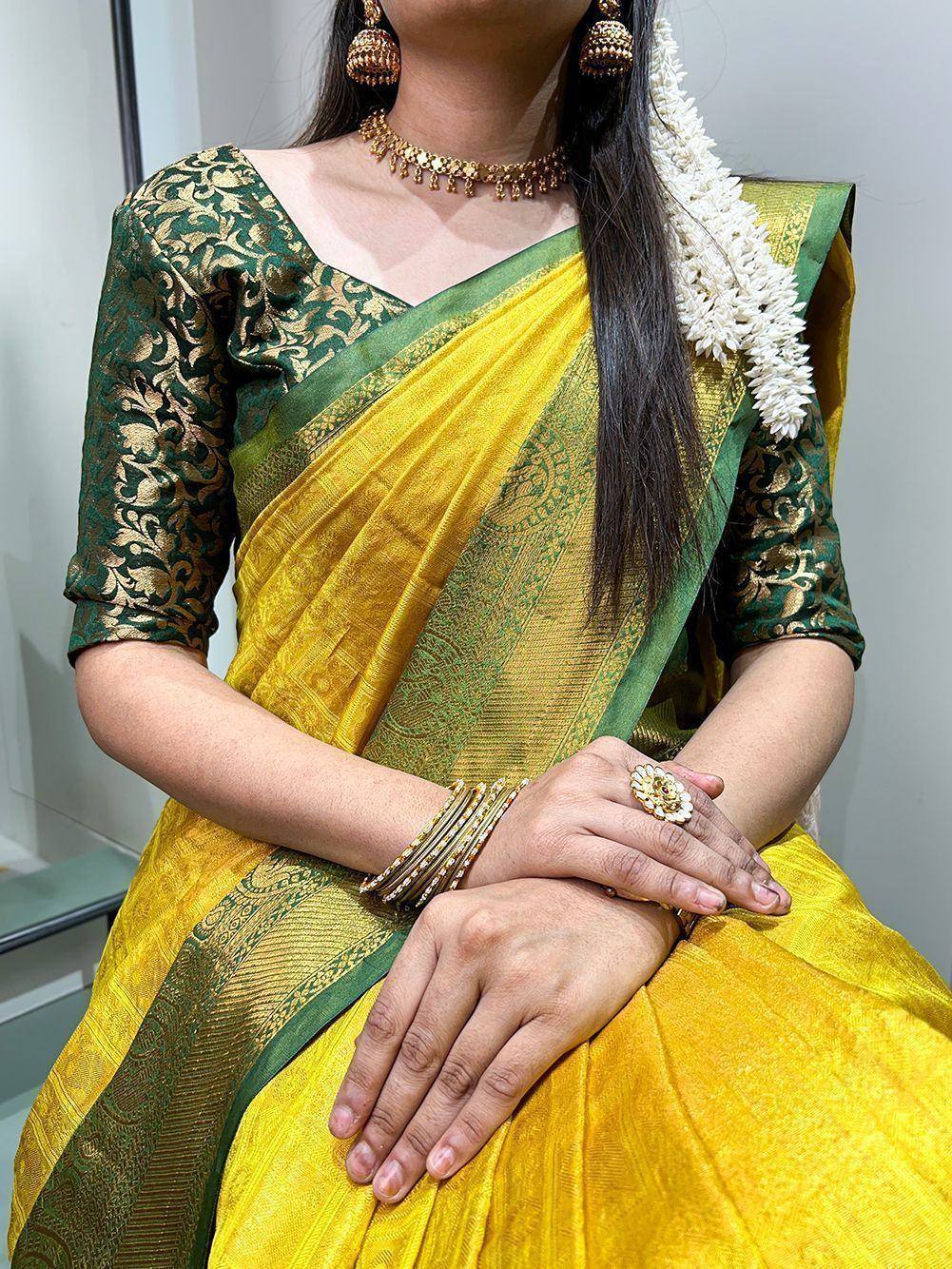 Yellow and green designer saree with gold embroidery, traditional jewelry, and floral hair accessory
