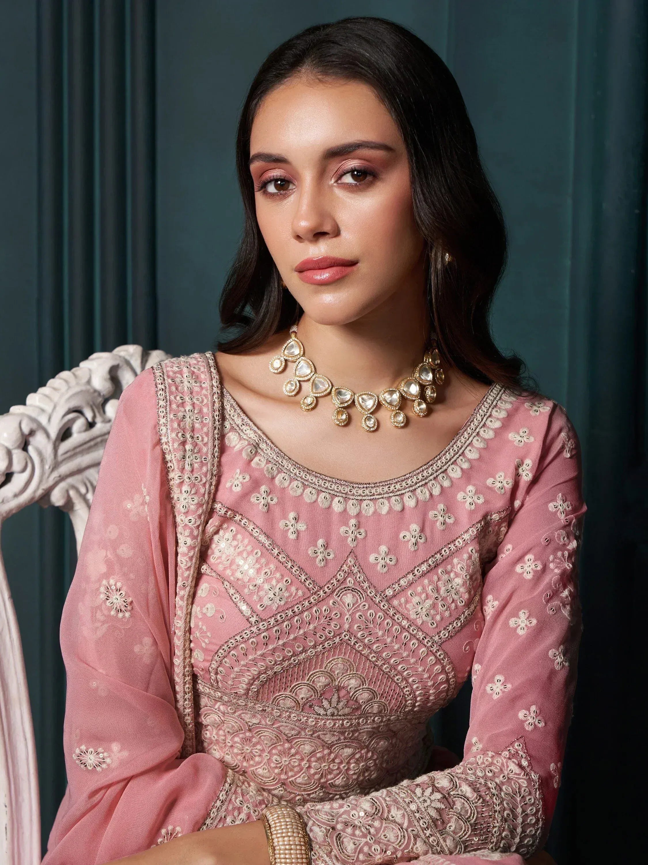 Elegant woman in pink embroidered salwar kameez with gold jewelry, styled for ethnic wear.