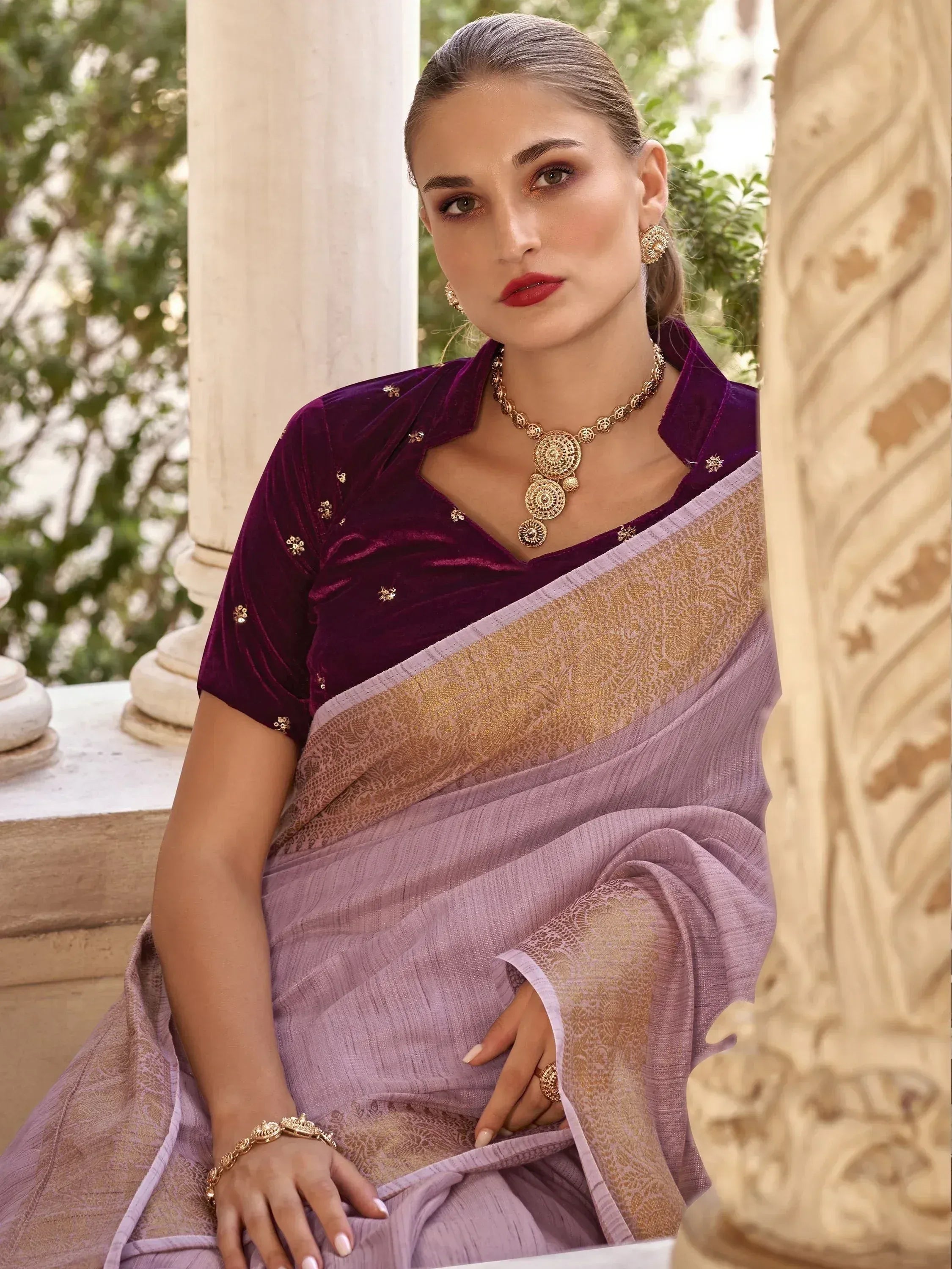 Woman in purple velvet blouse and lavender saree with gold embroidery, styled with traditional Indian jewelry