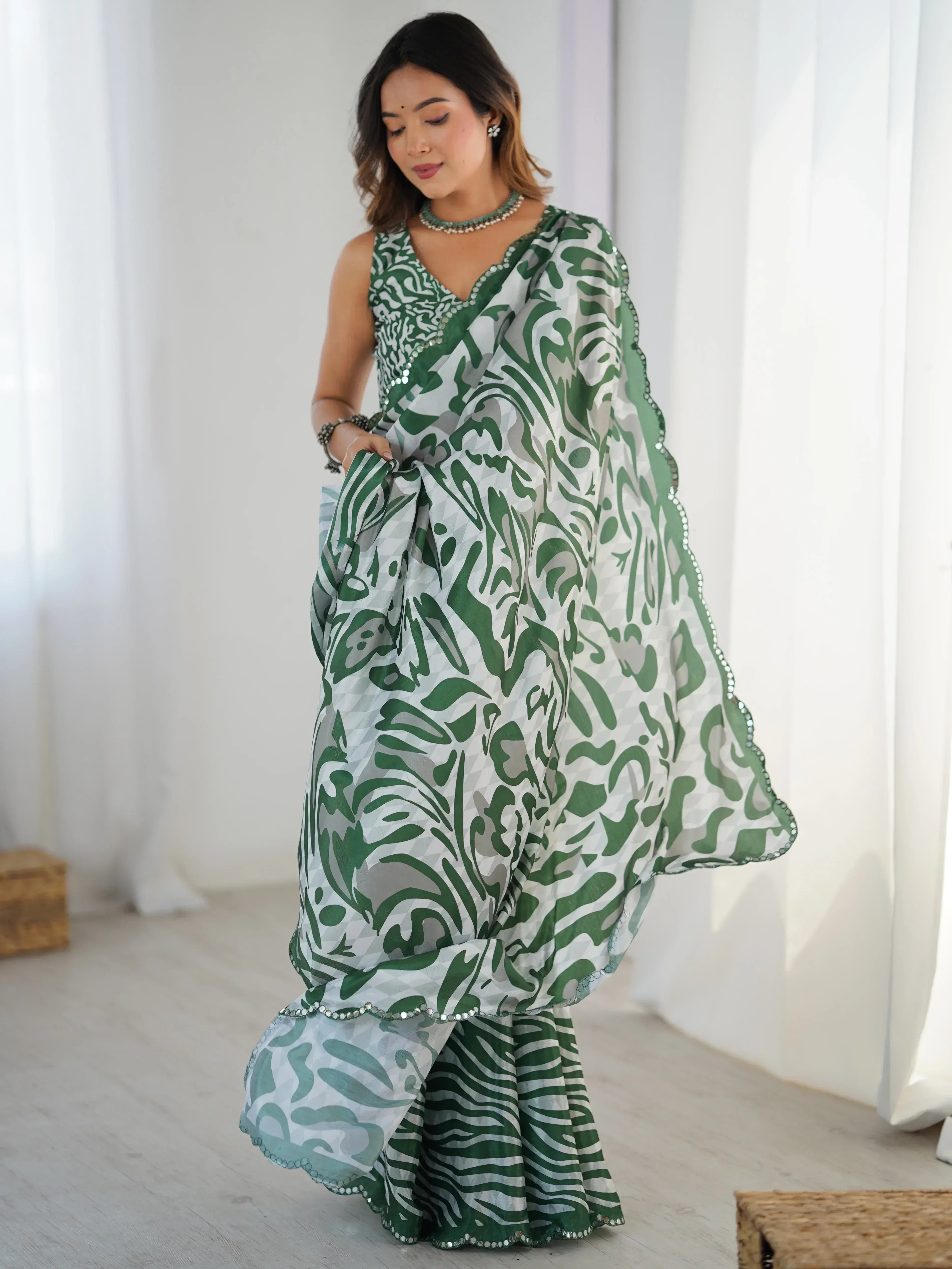 Green and white printed saree with abstract patterns, paired with a matching blouse and pearl necklace.