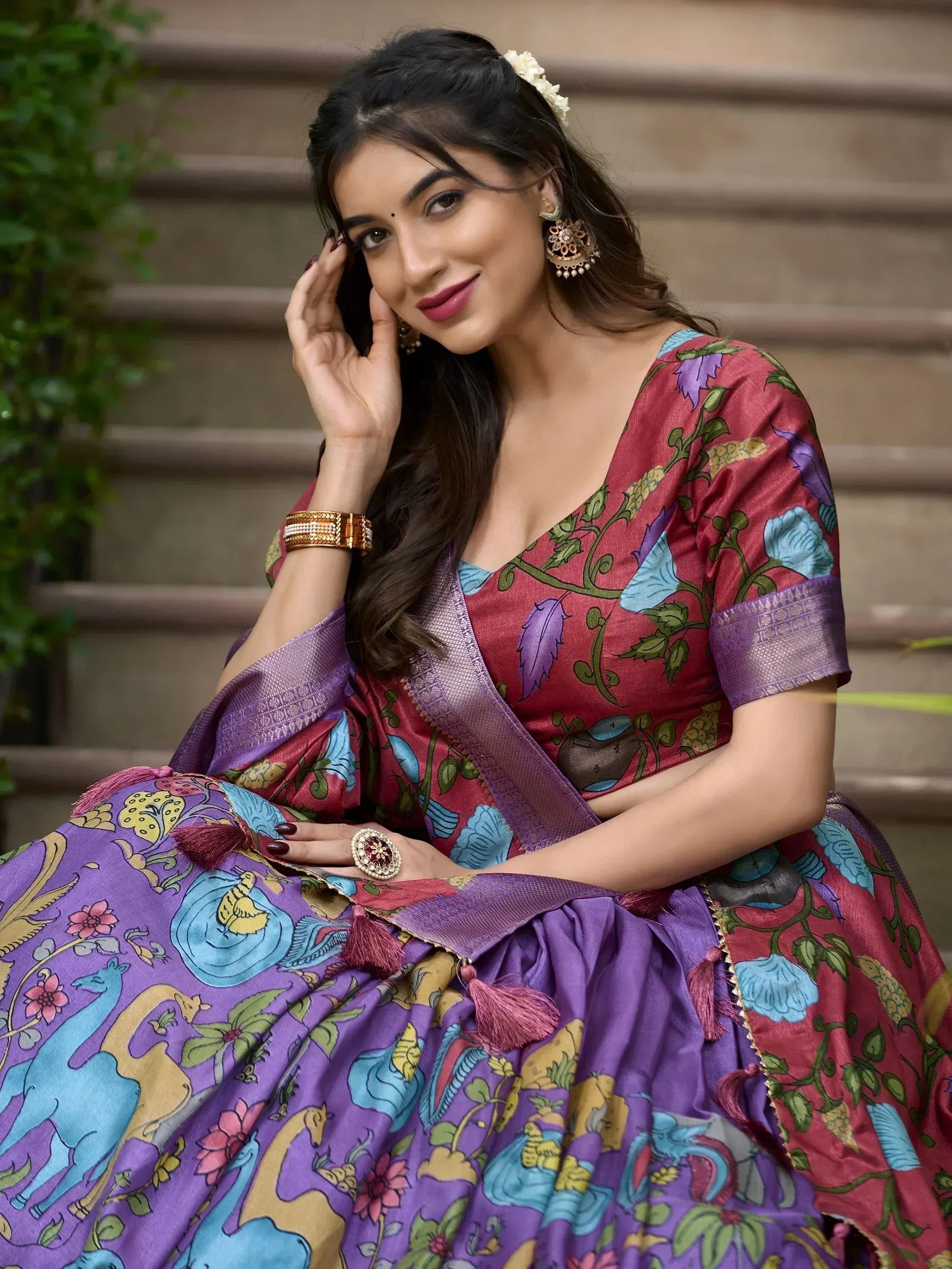 Woman in vibrant purple and red floral printed lehenga choli with tassels, styled with gold jewelry for ethnic occasions