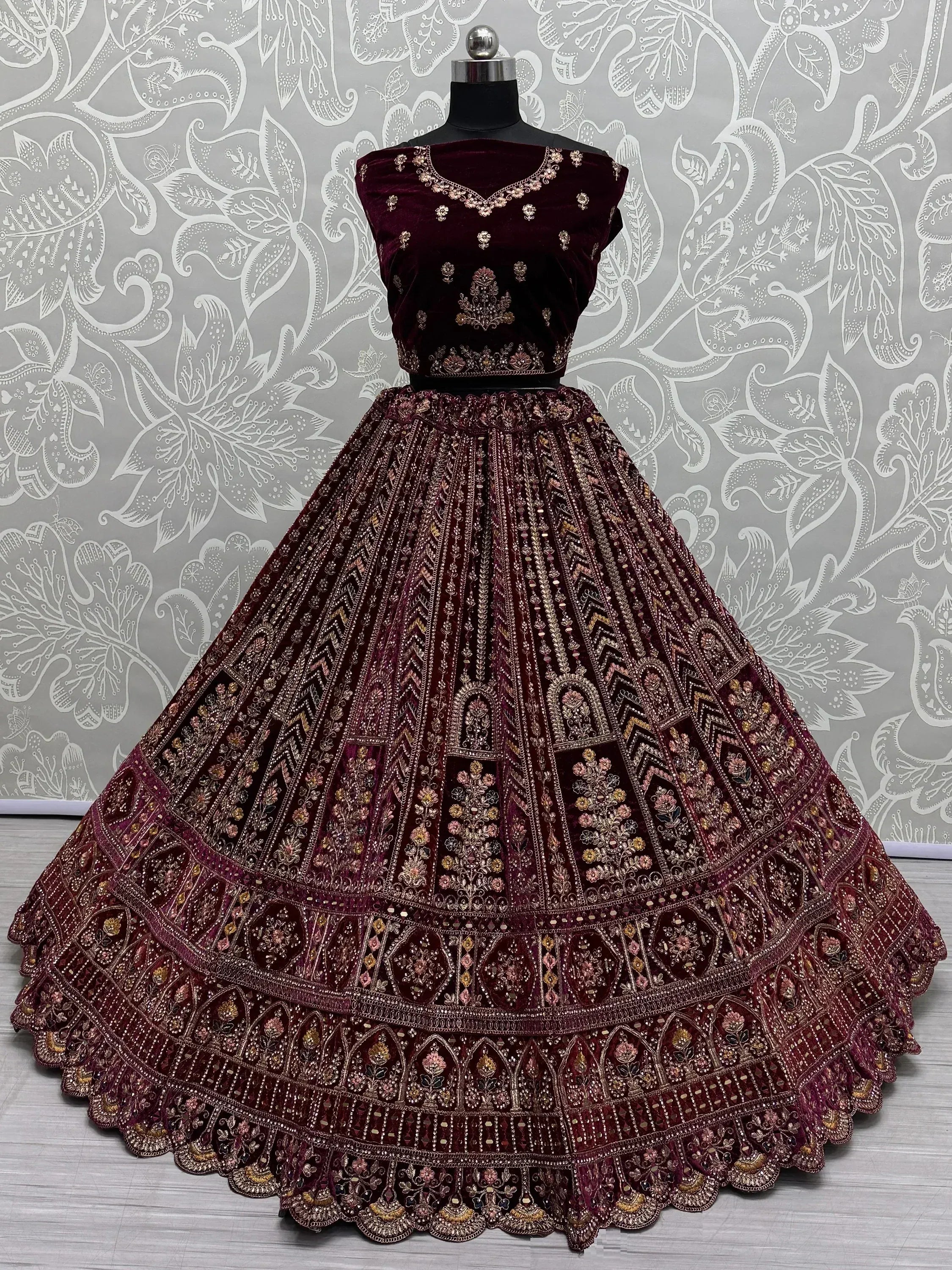 Burgundy velvet lehenga choli with intricate gold embroidery and floral motifs, displayed on mannequin