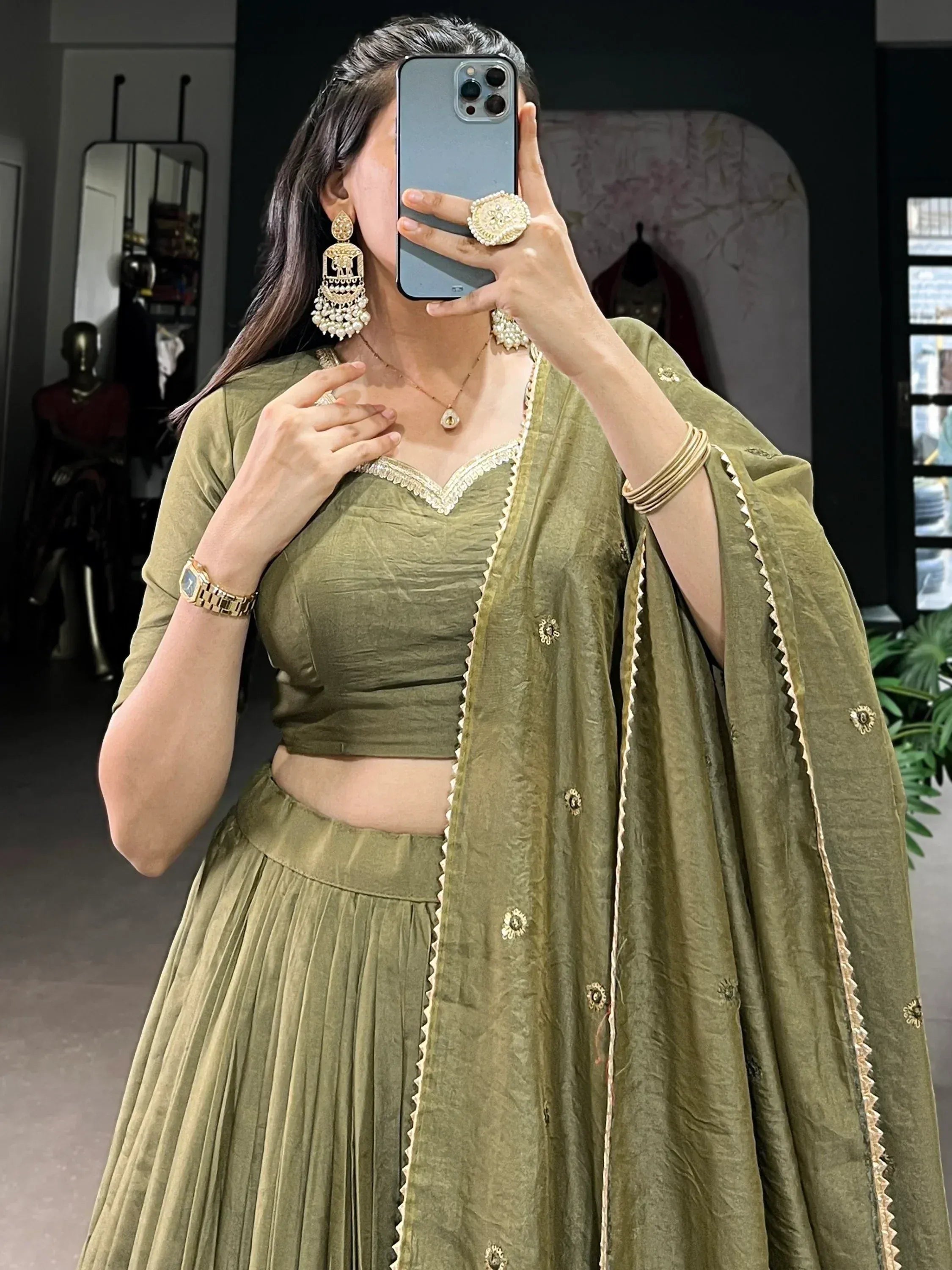 Olive green designer lehenga choli with gold embroidery, paired with statement earrings and traditional jewelry.