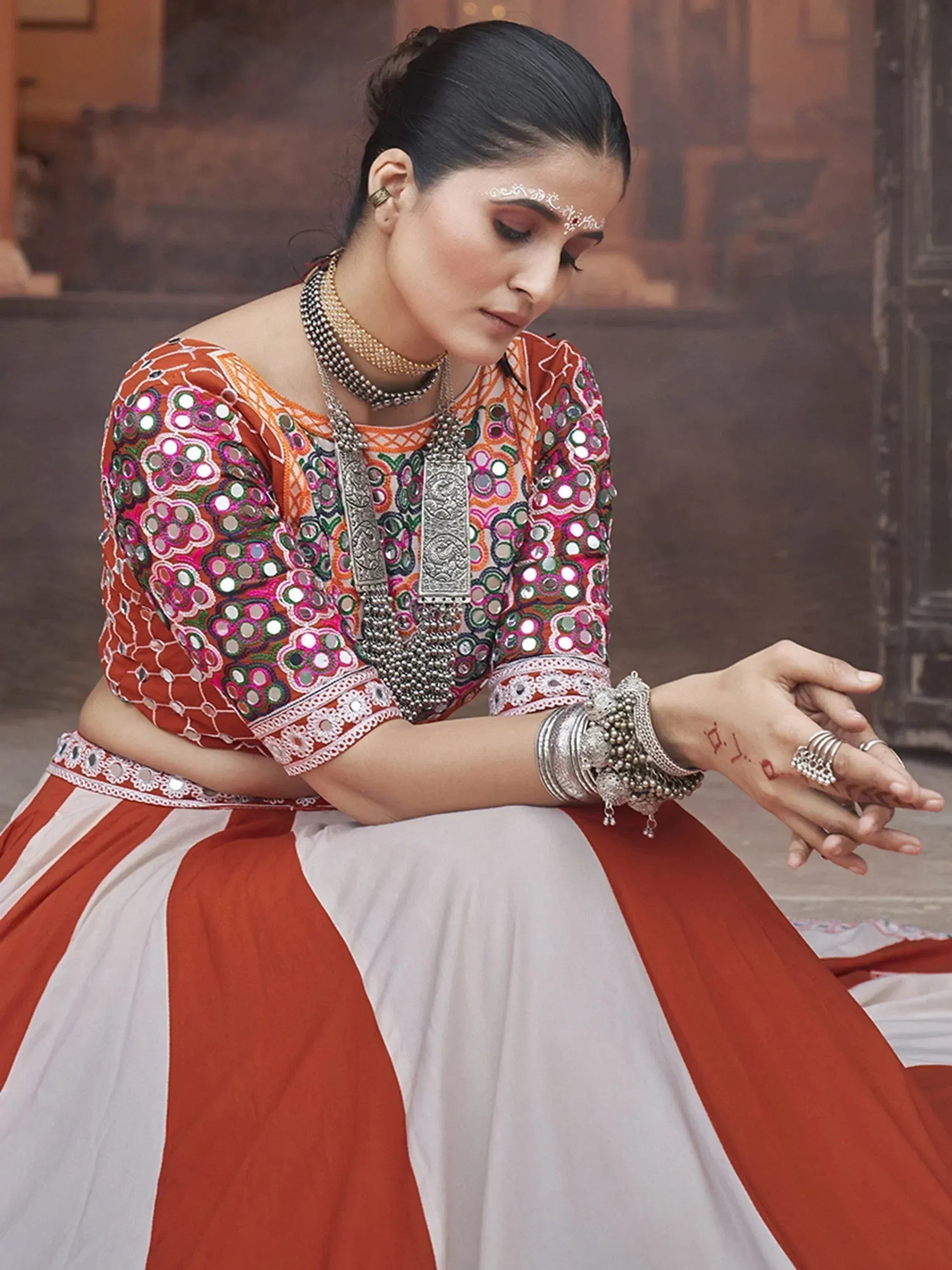 Woman in vibrant orange and white mirror-work ethnic lehenga choli with traditional silver jewelry