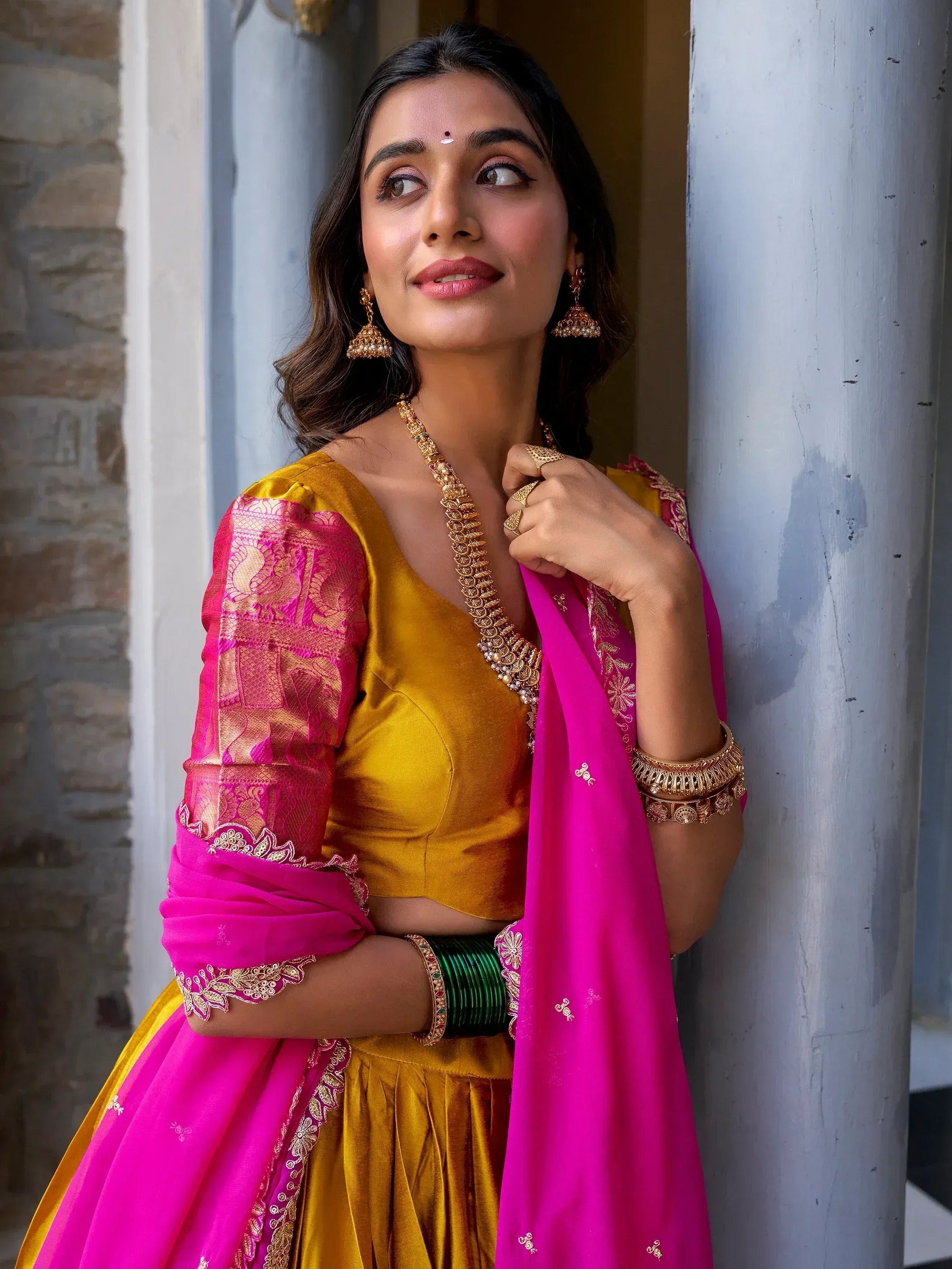 Woman in vibrant yellow and pink designer lehenga choli with gold embroidery, traditional Indian ethnic wear
