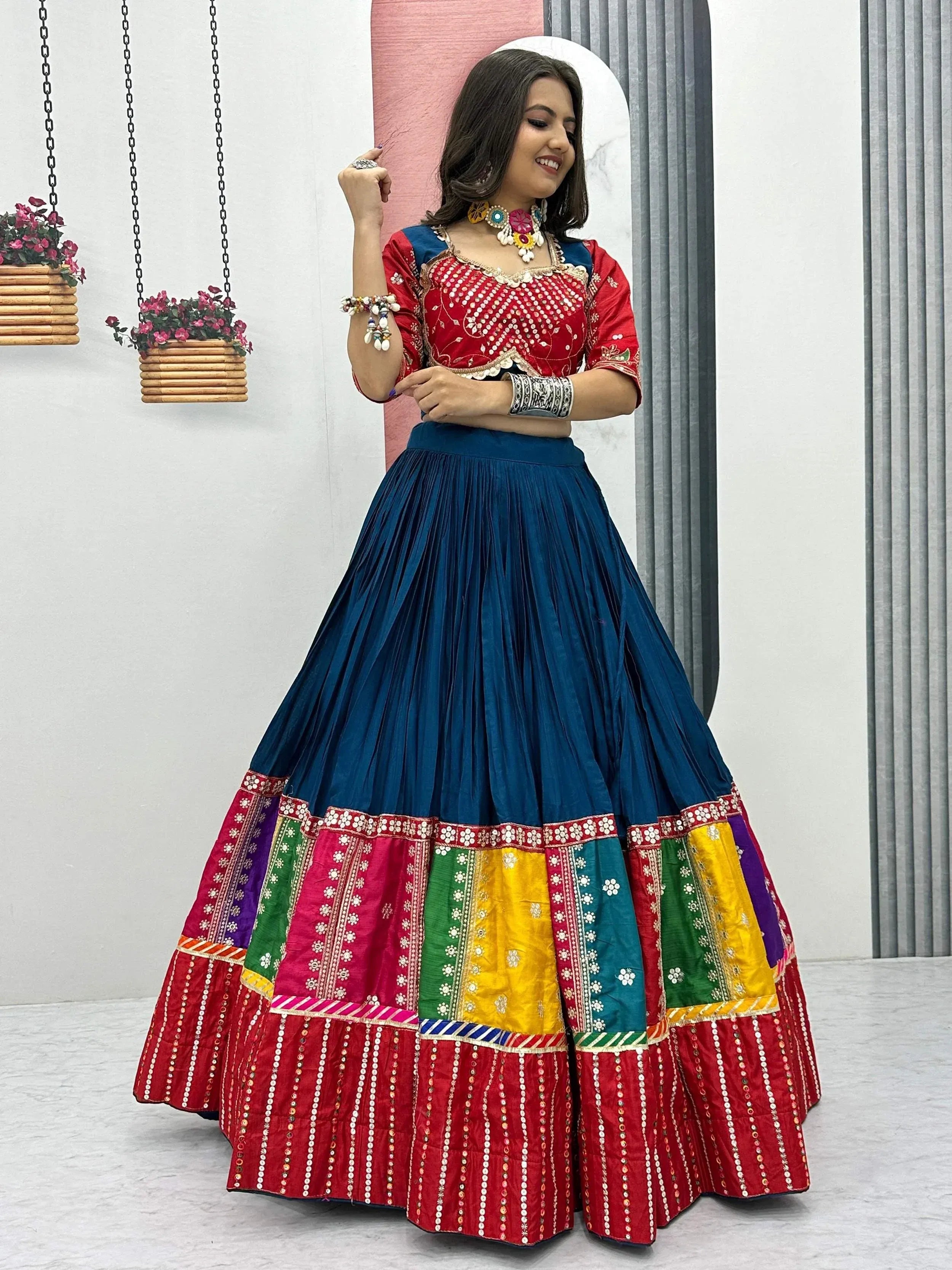 Woman in vibrant red and blue embroidered lehenga choli with colorful patchwork skirt, perfect for Indian ethnic wear.