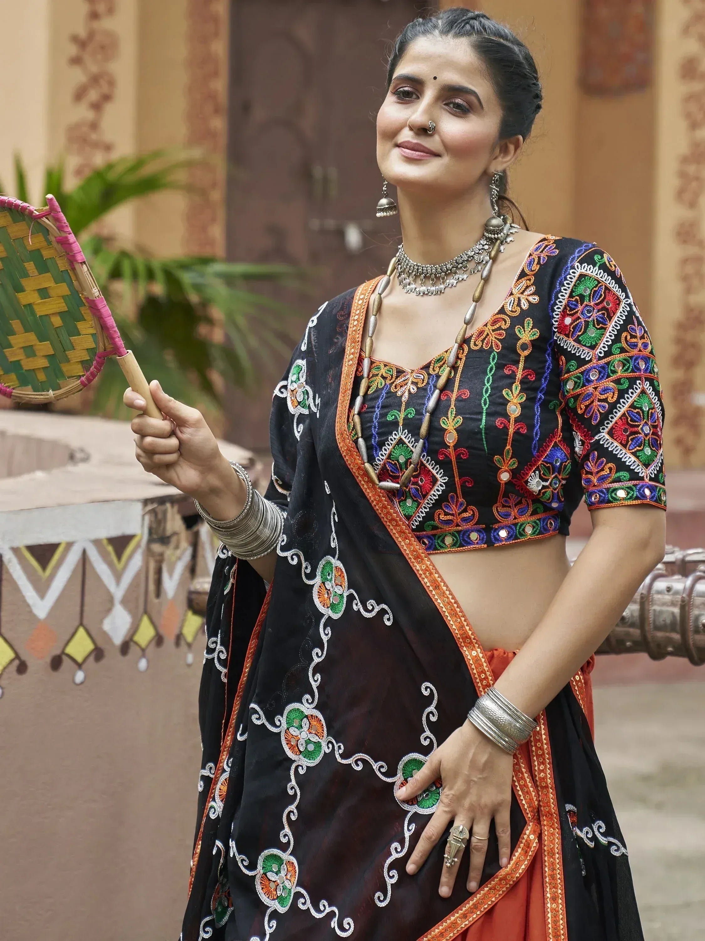 Woman in black embroidered lehenga choli with mirror work, holding fan, traditional Indian ethnic wear