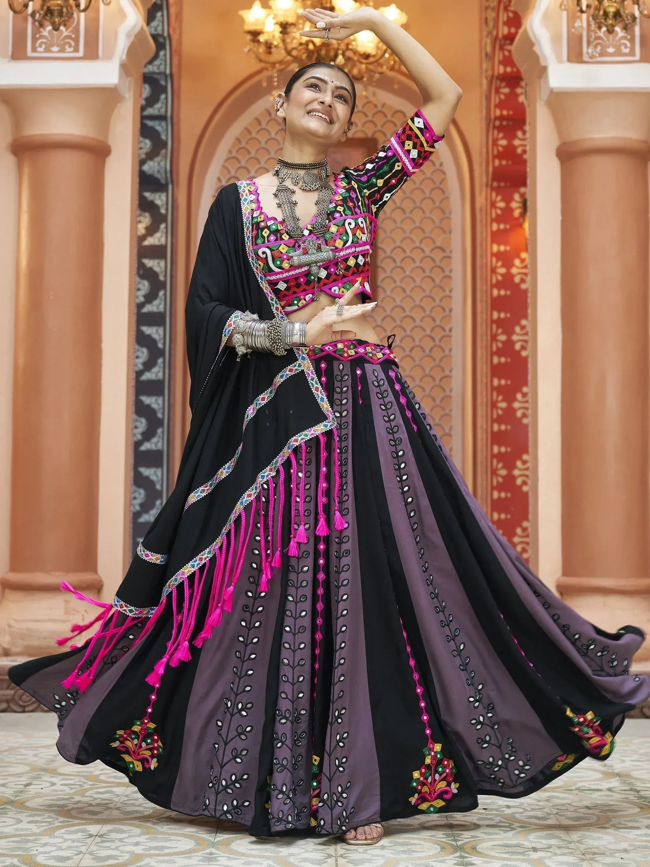 Woman in vibrant black and purple embroidered lehenga choli with mirror work, dancing in ornate Indian palace setting