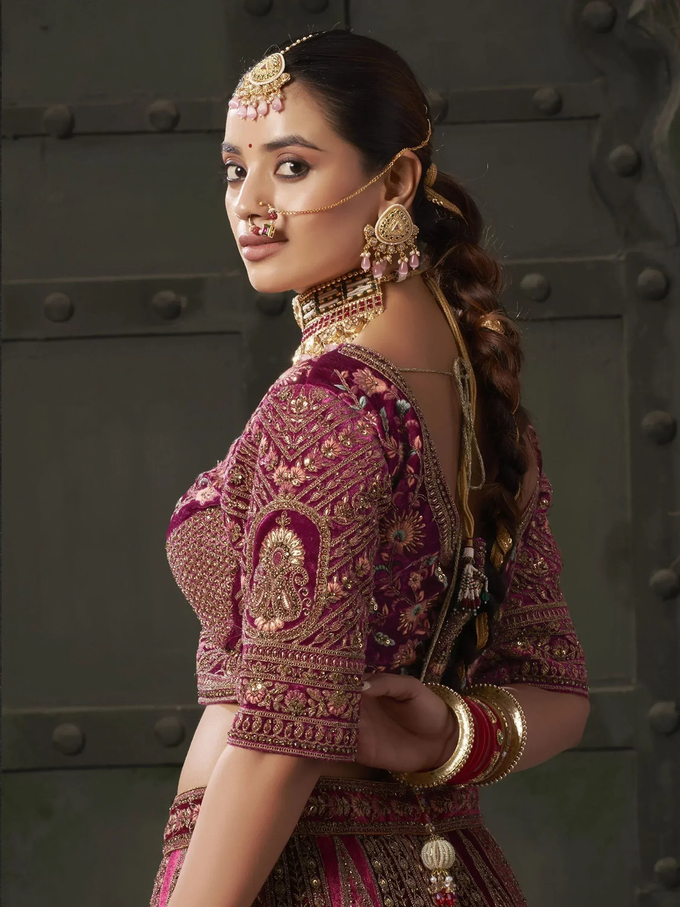 Woman in maroon embroidered lehenga choli with gold jewelry and traditional Indian bridal accessories