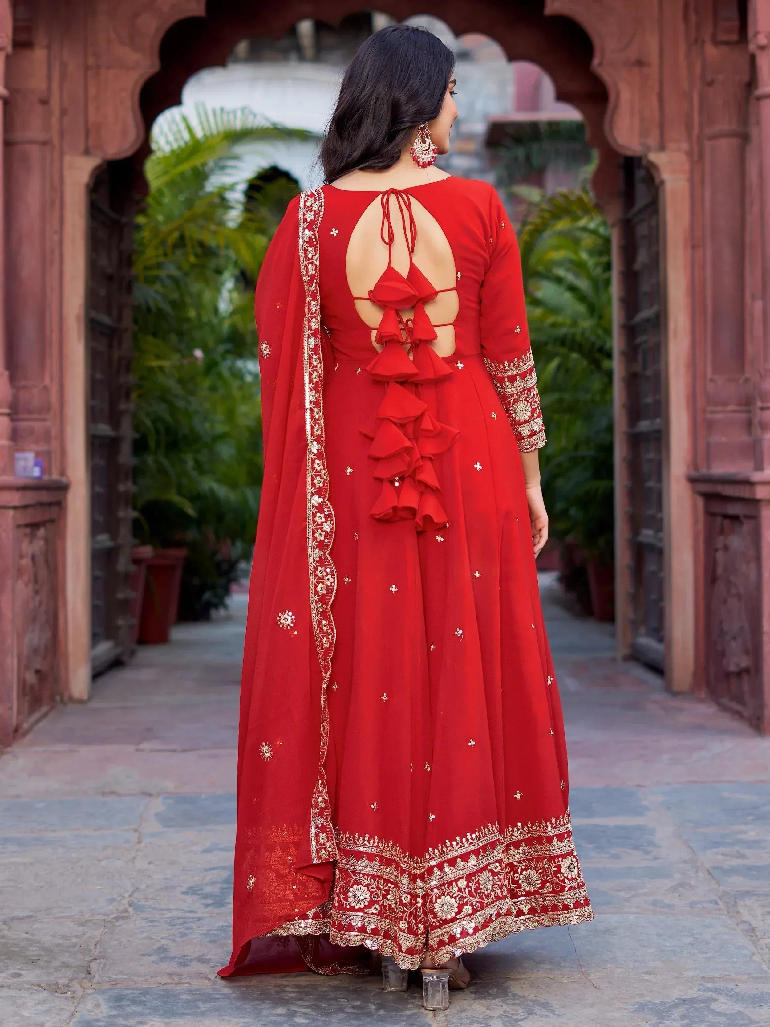Red ethnic gown with gold embroidery and back ruffle detailing, perfect for Indian celebrations.