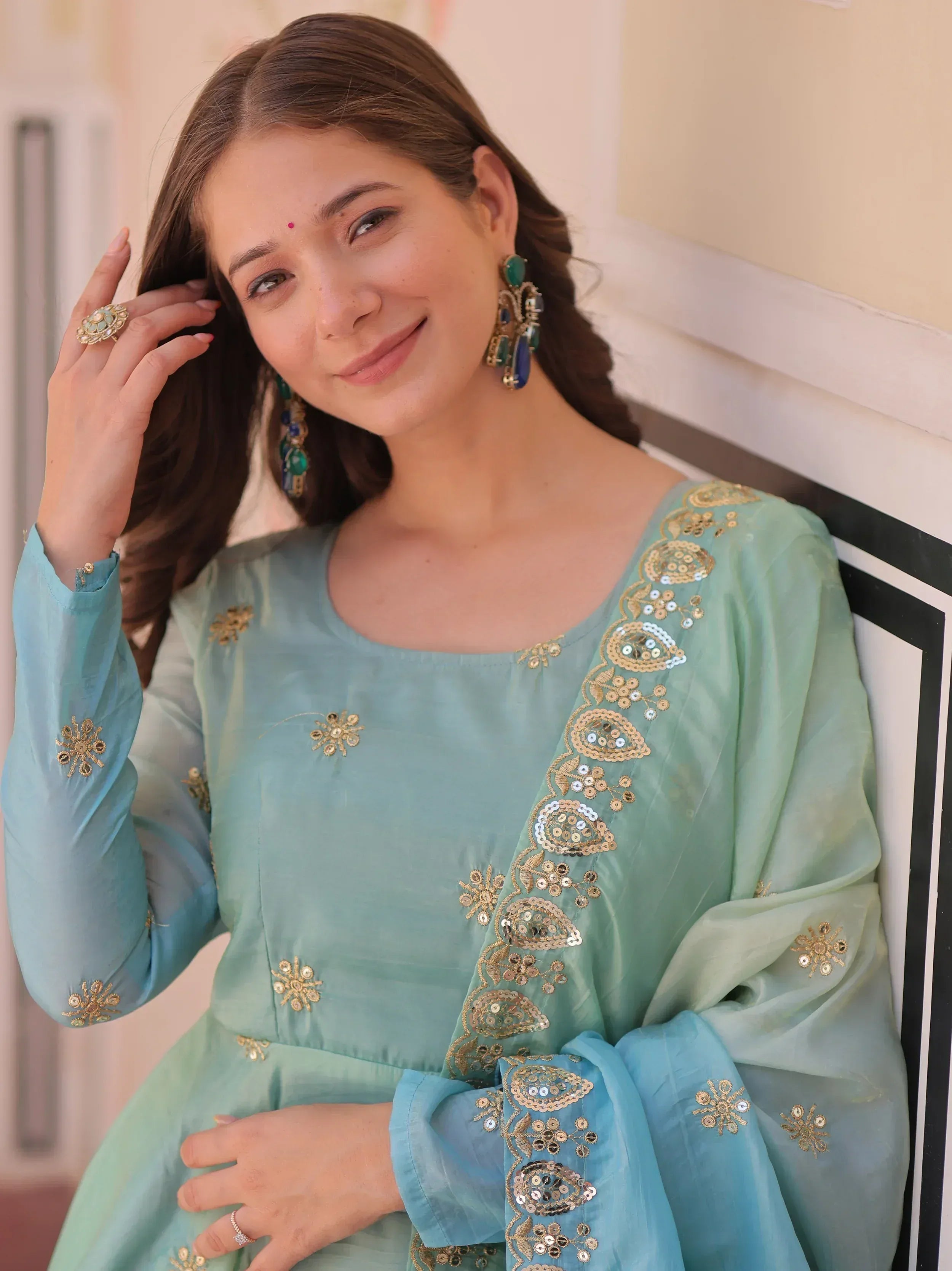 Woman in mint green embroidered salwar kameez with gold sequin work, matching dupatta, and statement earrings.