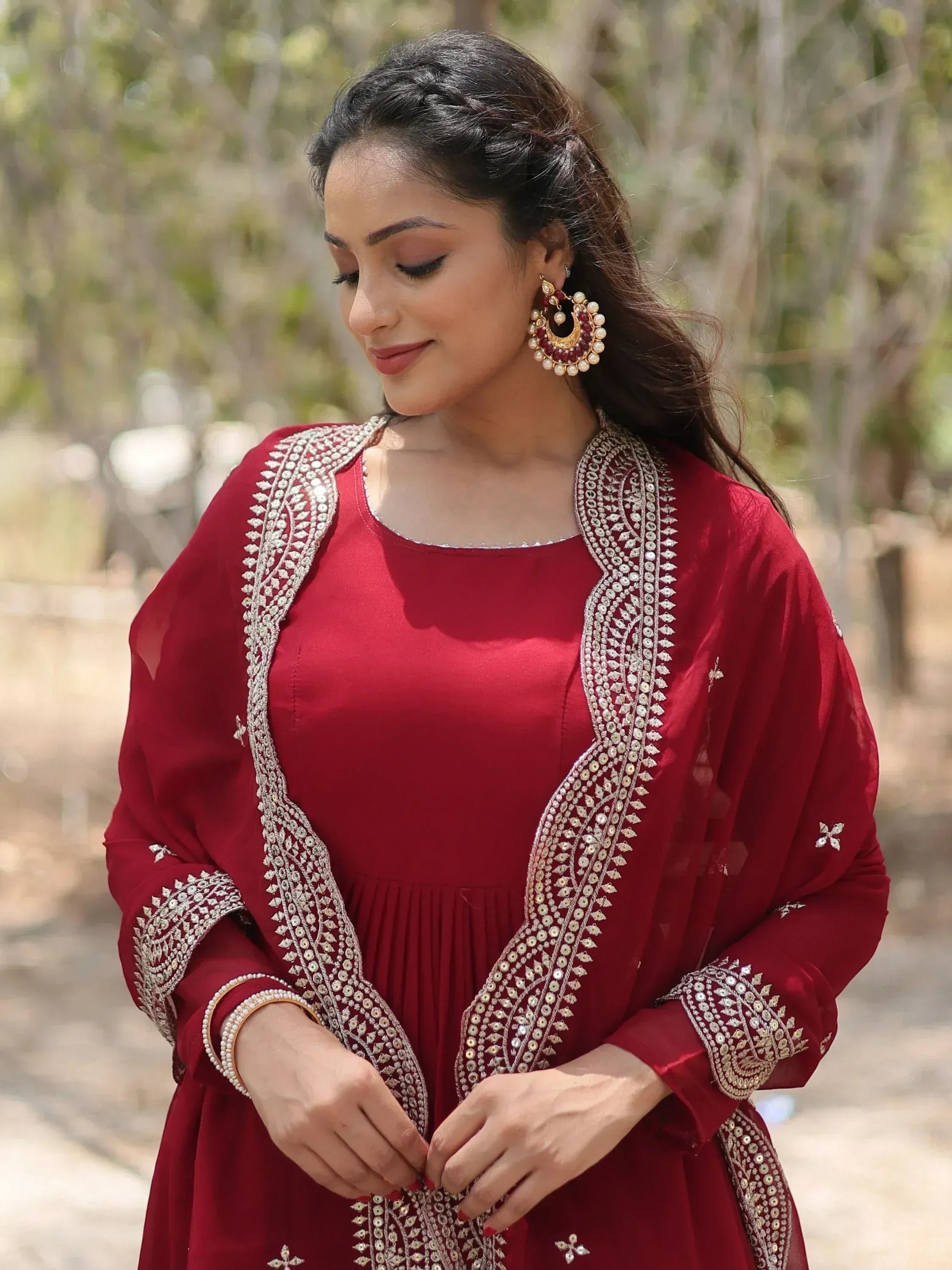Woman in maroon embroidered ethnic gown with dupatta and traditional jewelry outdoors