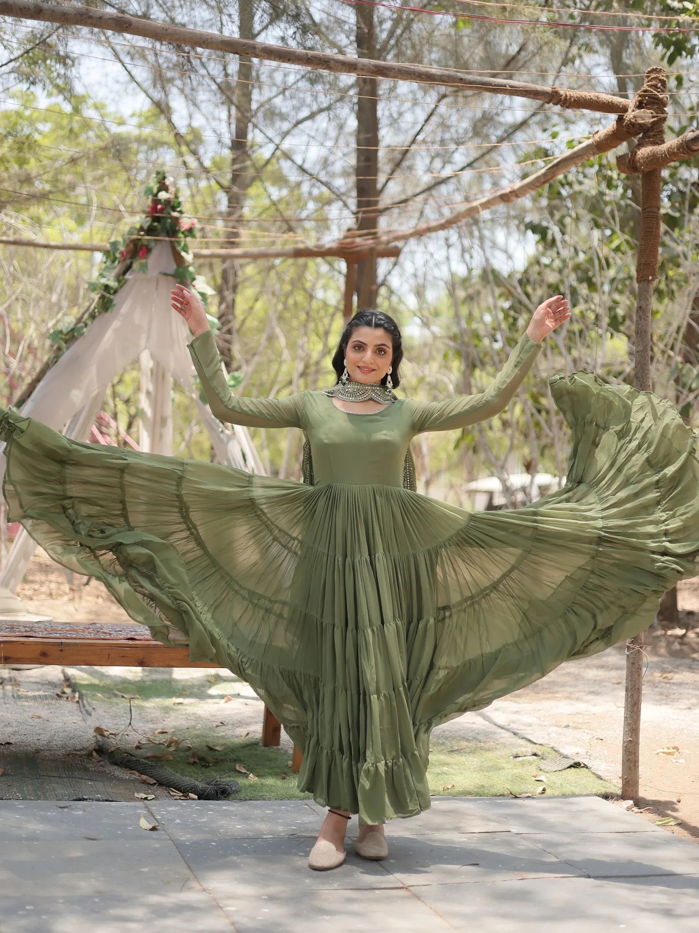 Woman in flowing olive green ethnic gown posing outdoors with dupatta and jewelry