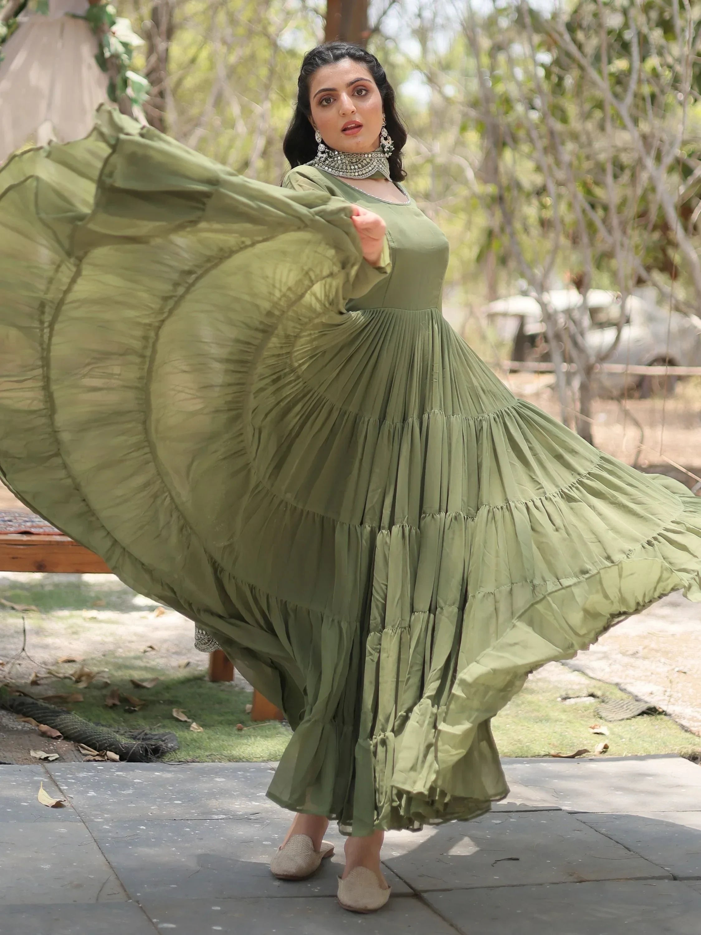 Woman twirling in olive green ethnic gown with statement jewelry outdoors