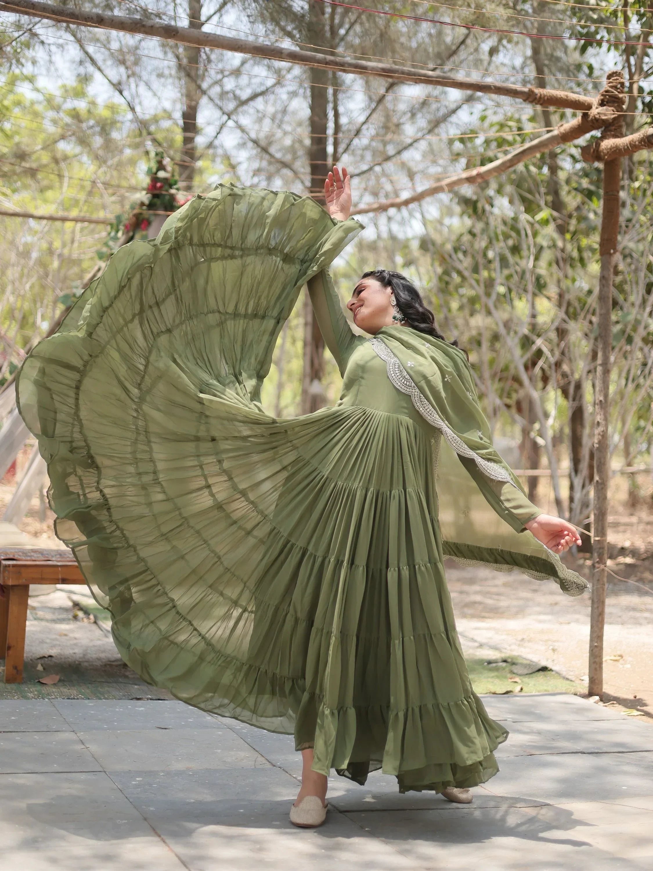 Woman twirling in an olive green ethnic gown outdoors, flowing dress with dupatta