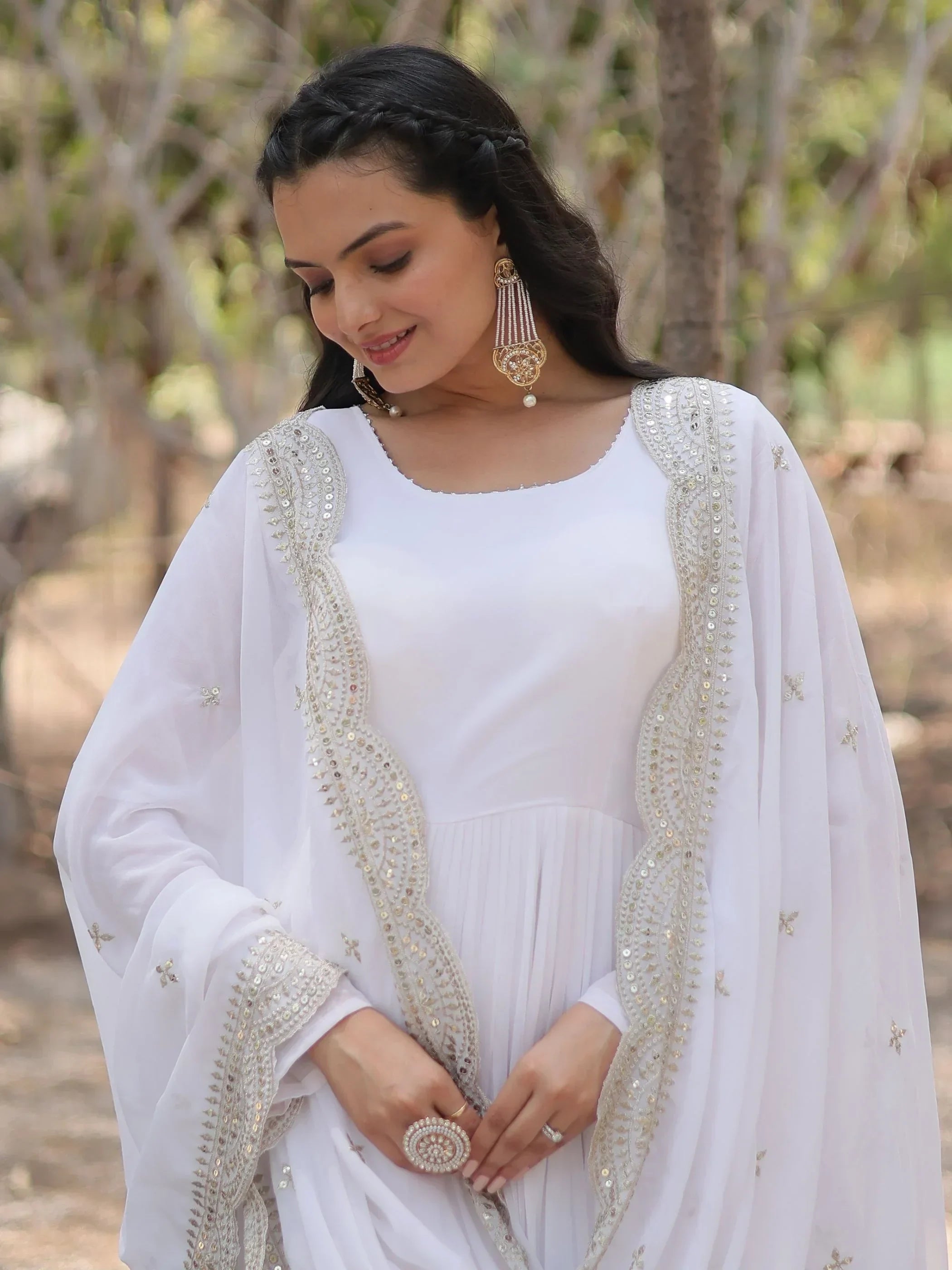 Woman wearing elegant white ethnic gown with gold embroidery and statement earrings outdoors