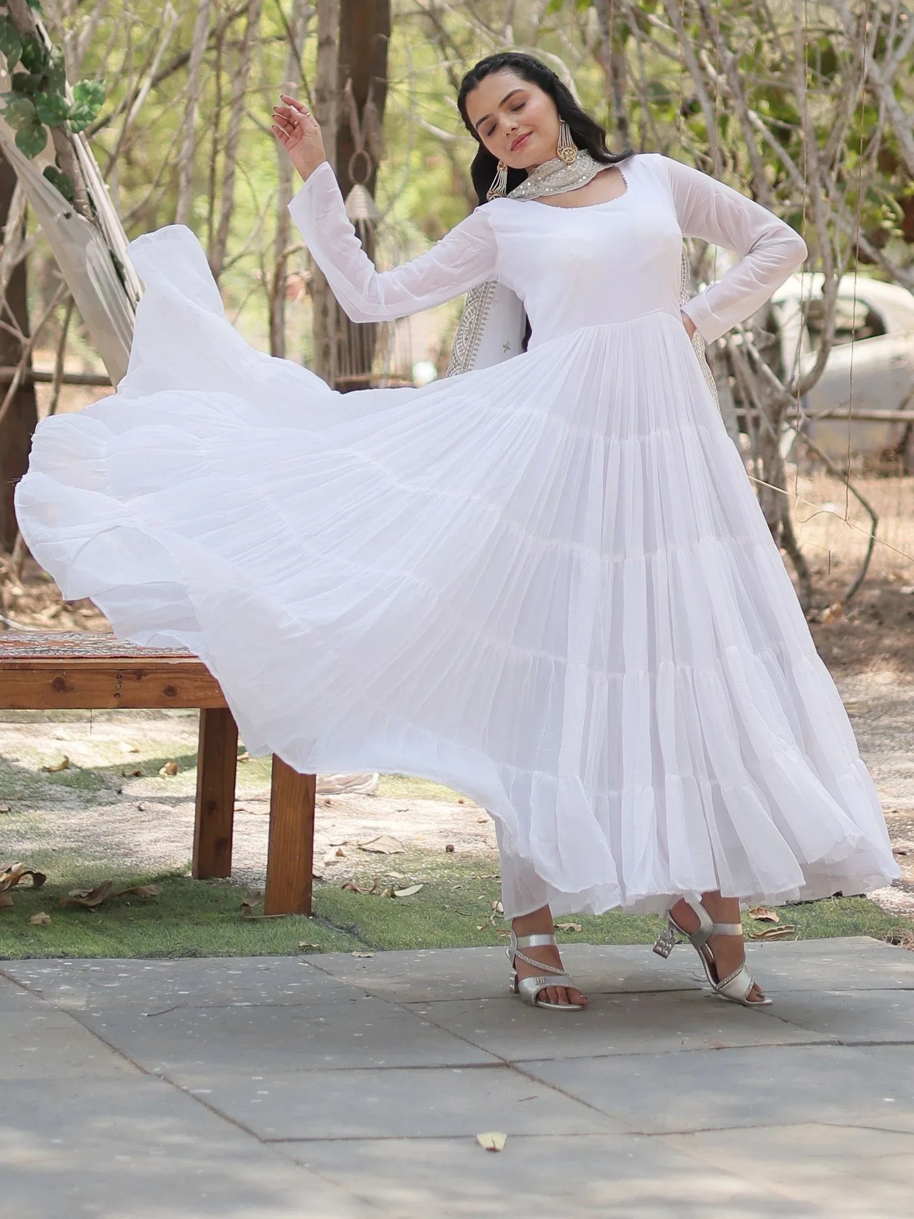 Woman twirling in a white long Anarkali dress with silver dupatta outdoors