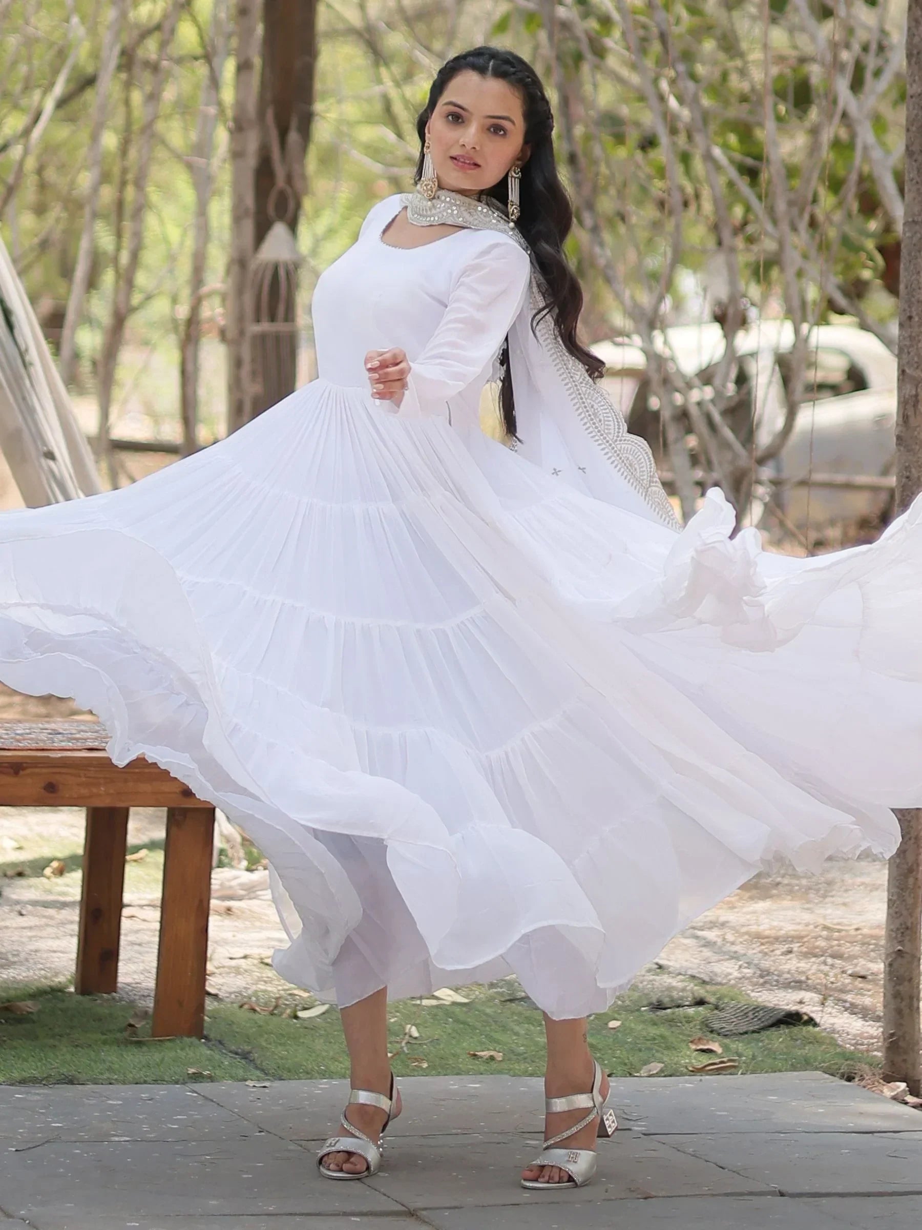 Woman twirling in a long white anarkali dress with dupatta and statement earrings outdoors