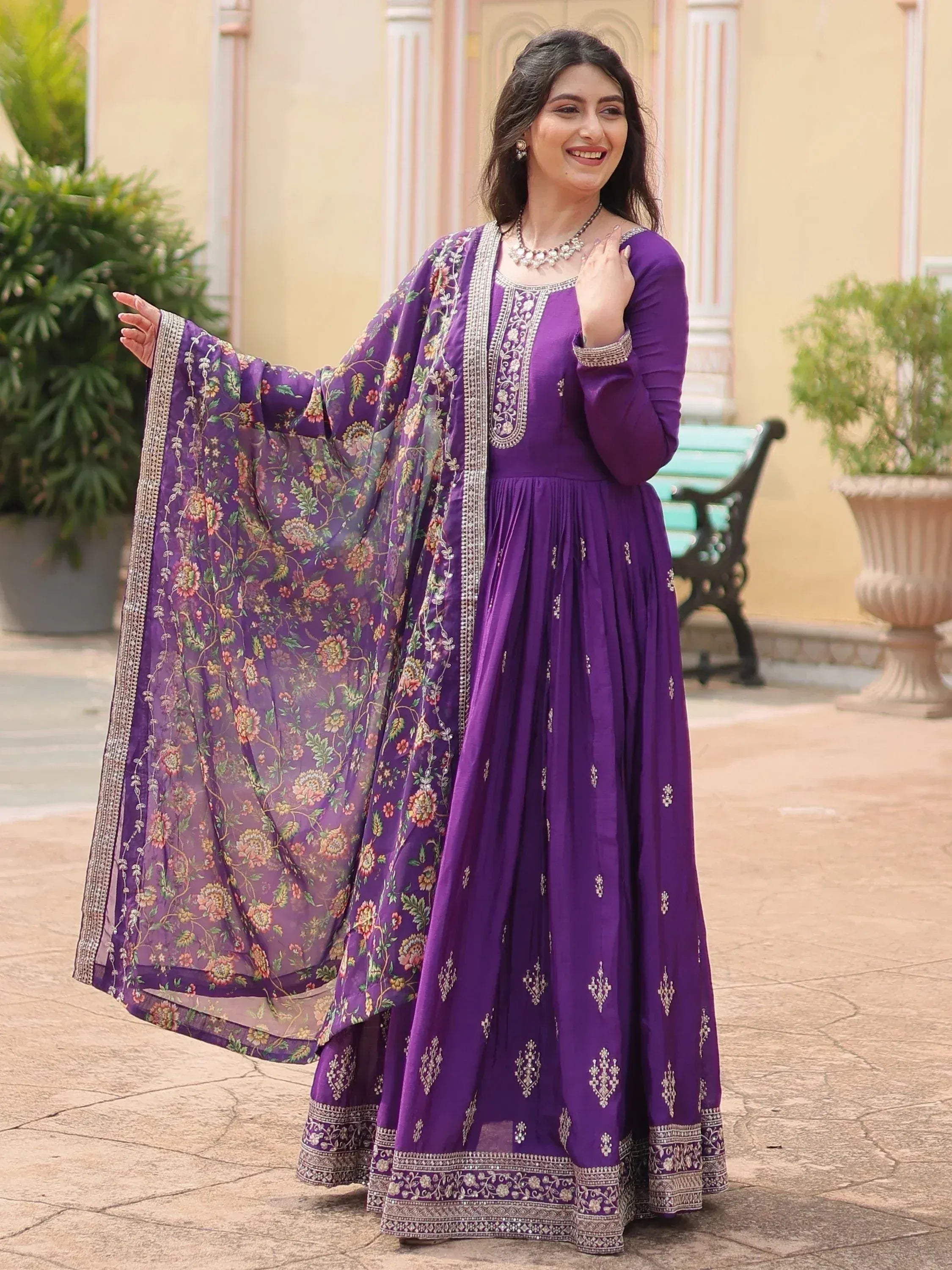Woman wearing a purple embroidered Anarkali suit with matching floral dupatta outdoors
