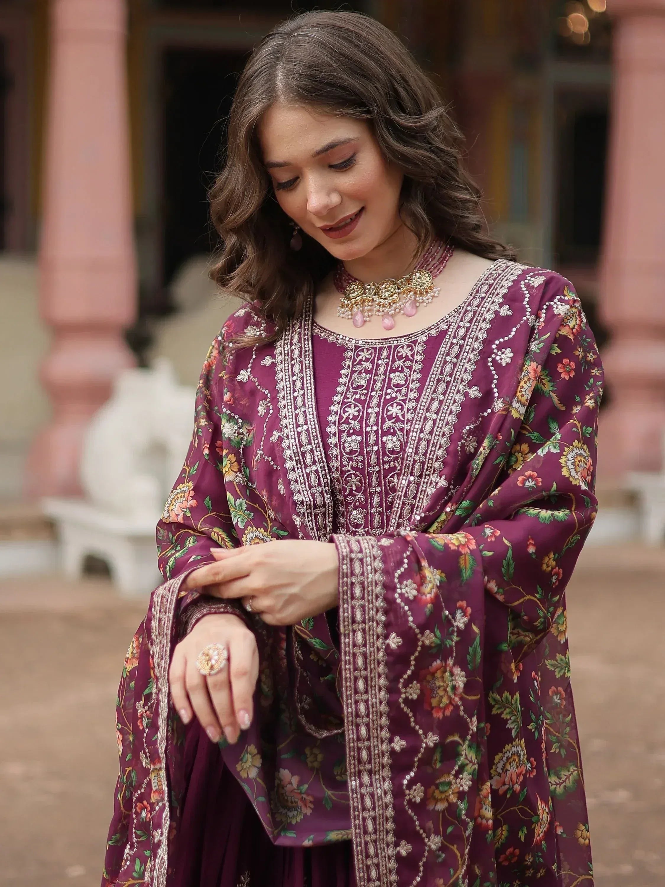 Woman wearing a wine-colored embroidered ethnic suit with floral dupatta and jewelry
