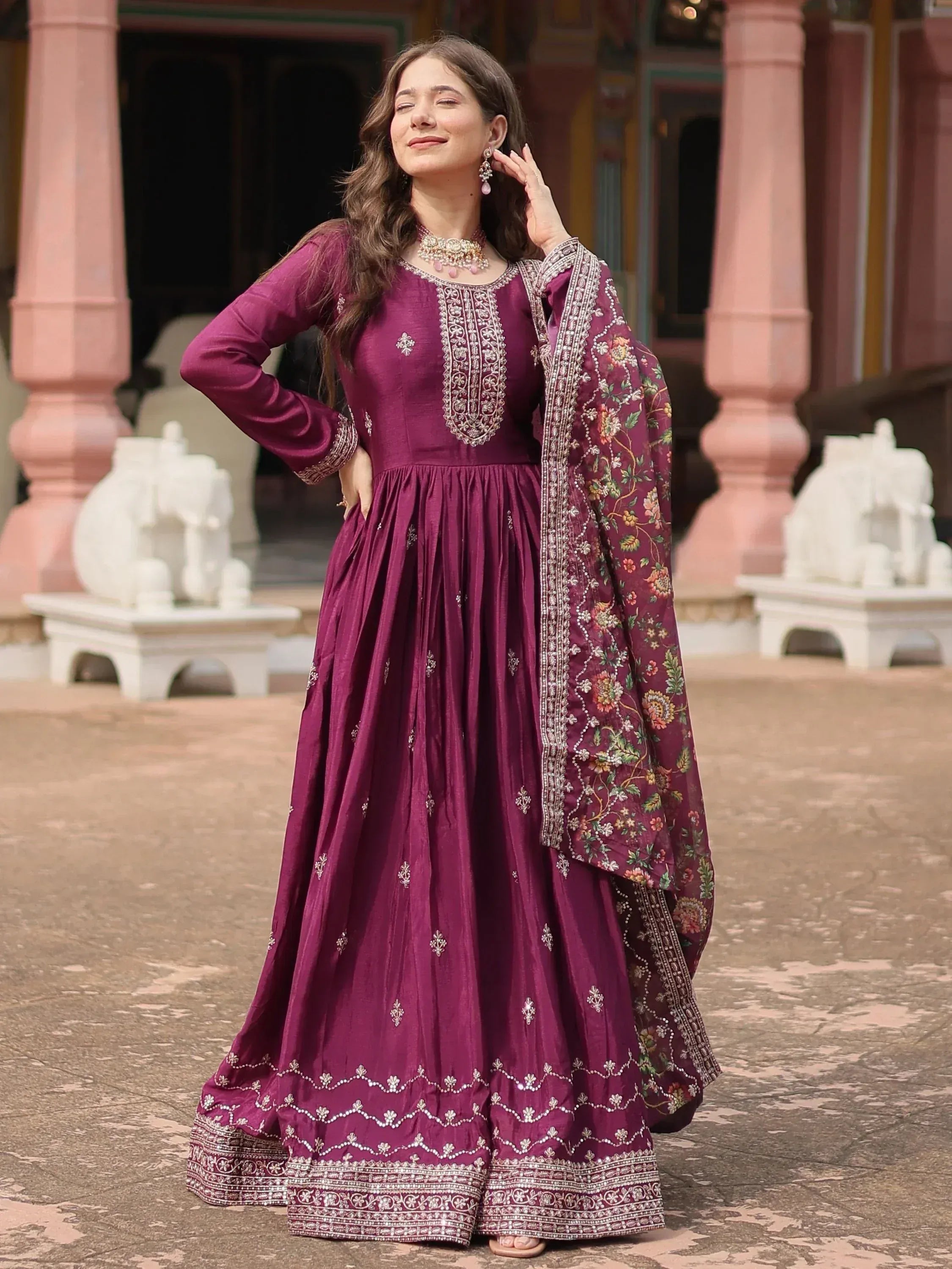 Woman in wine-colored ethnic gown with embroidered dupatta, standing outdoors