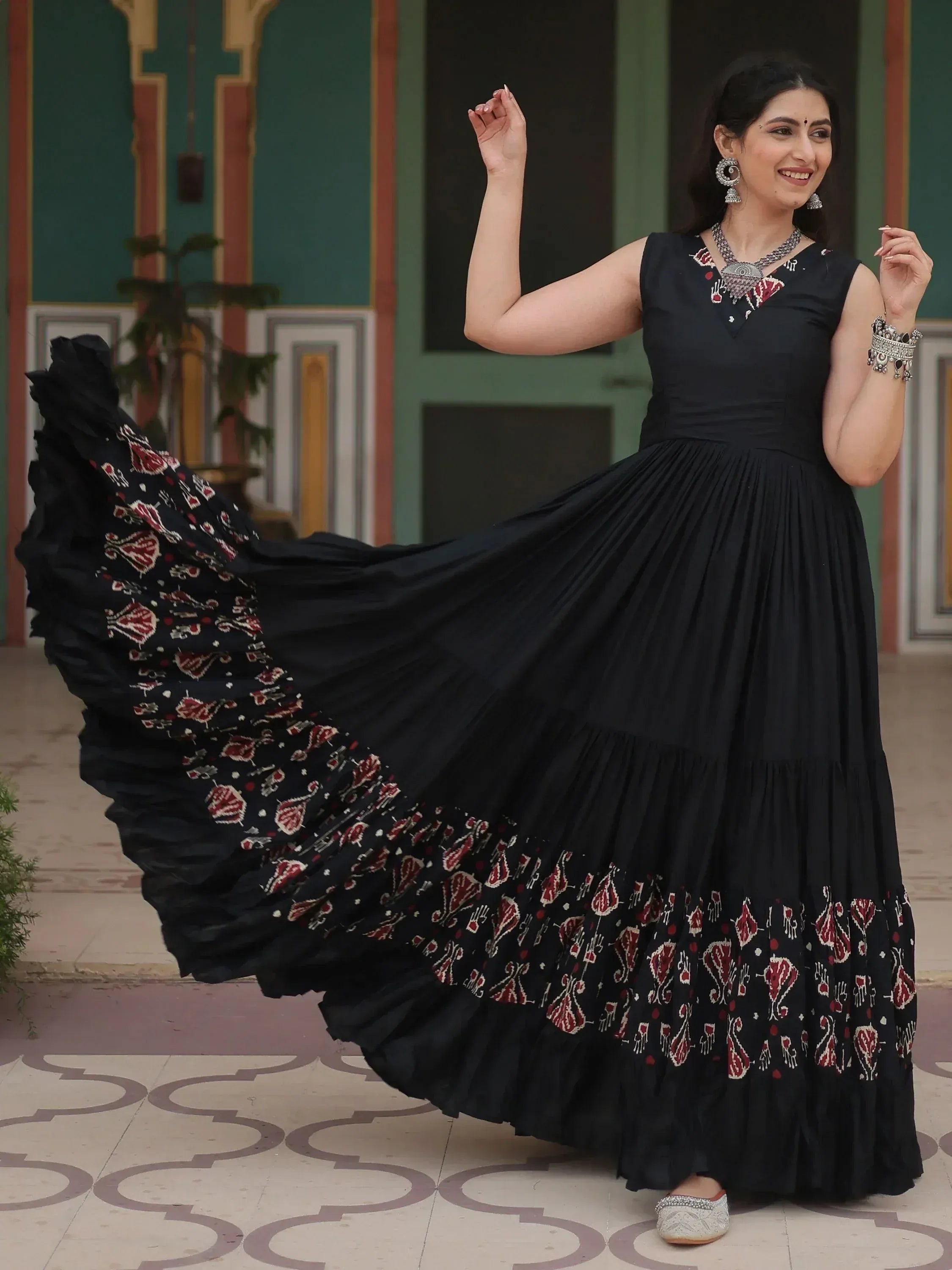 Black ethnic gown with red paisley print, pleated skirt, and traditional jewelry for festive occasions
