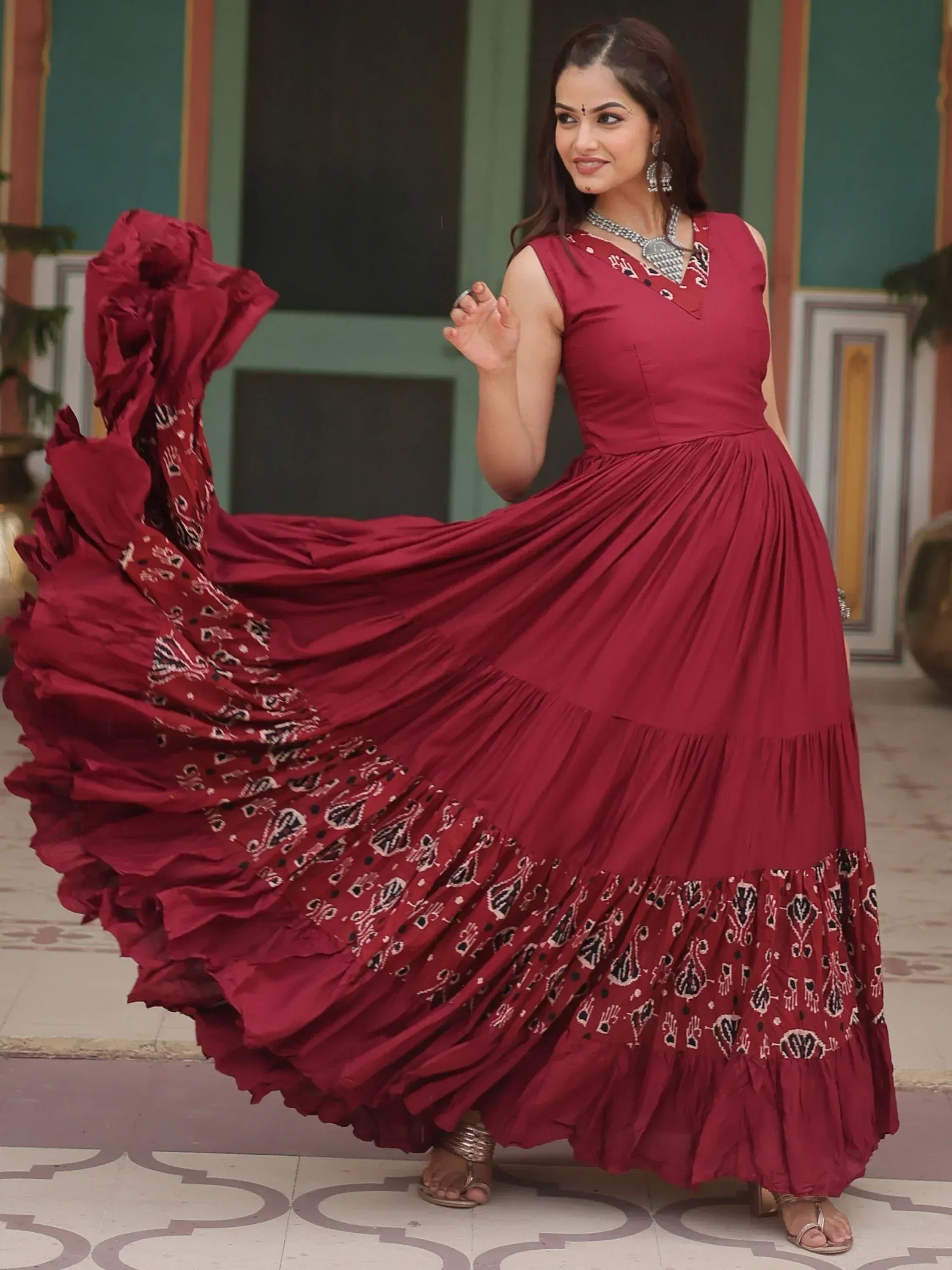 Woman twirling in maroon ethnic gown with printed ruffles, perfect for Indian occasions and festive wear.