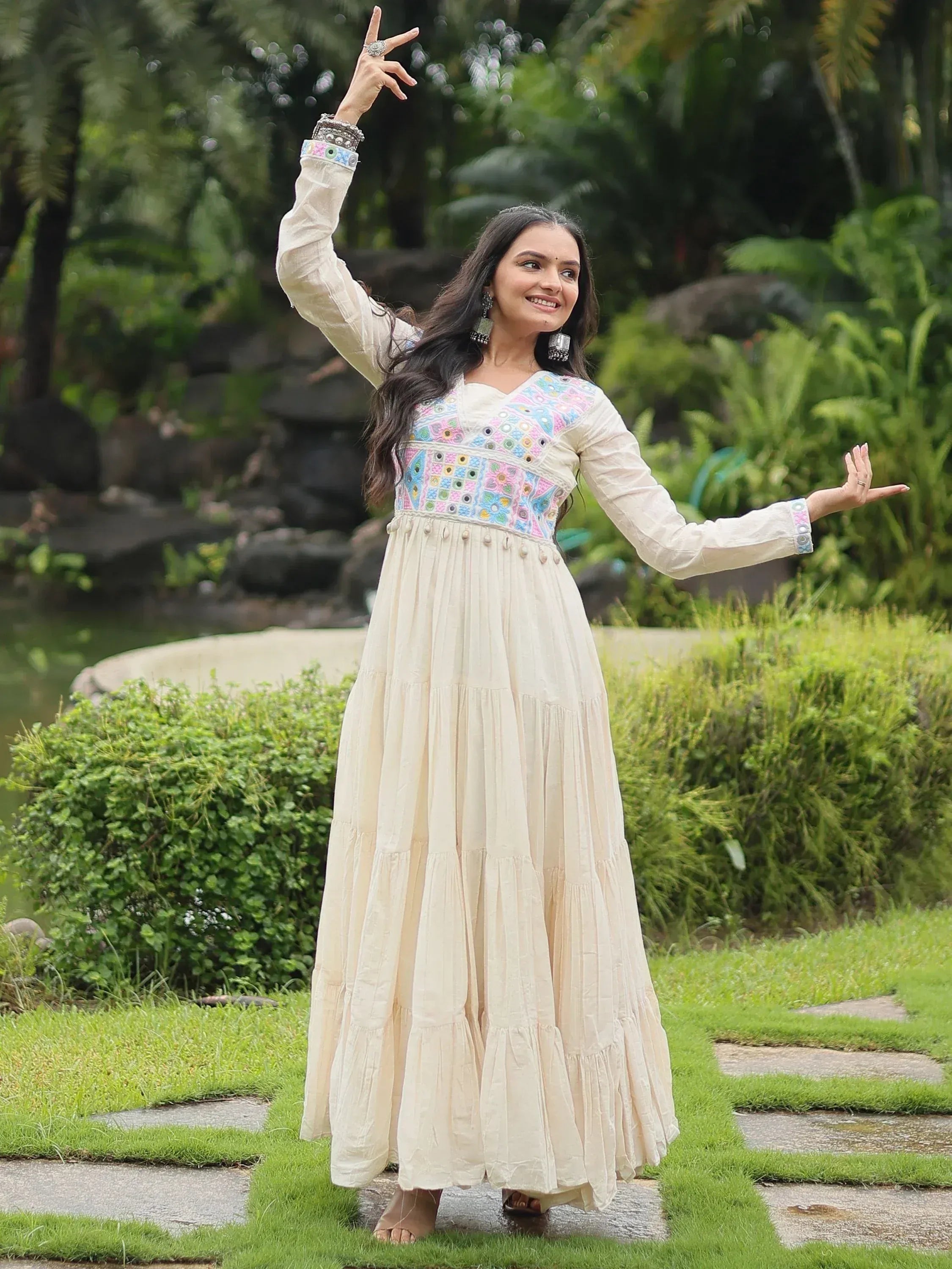 Woman in cream long ethnic gown with colorful embroidery, posing outdoors in garden