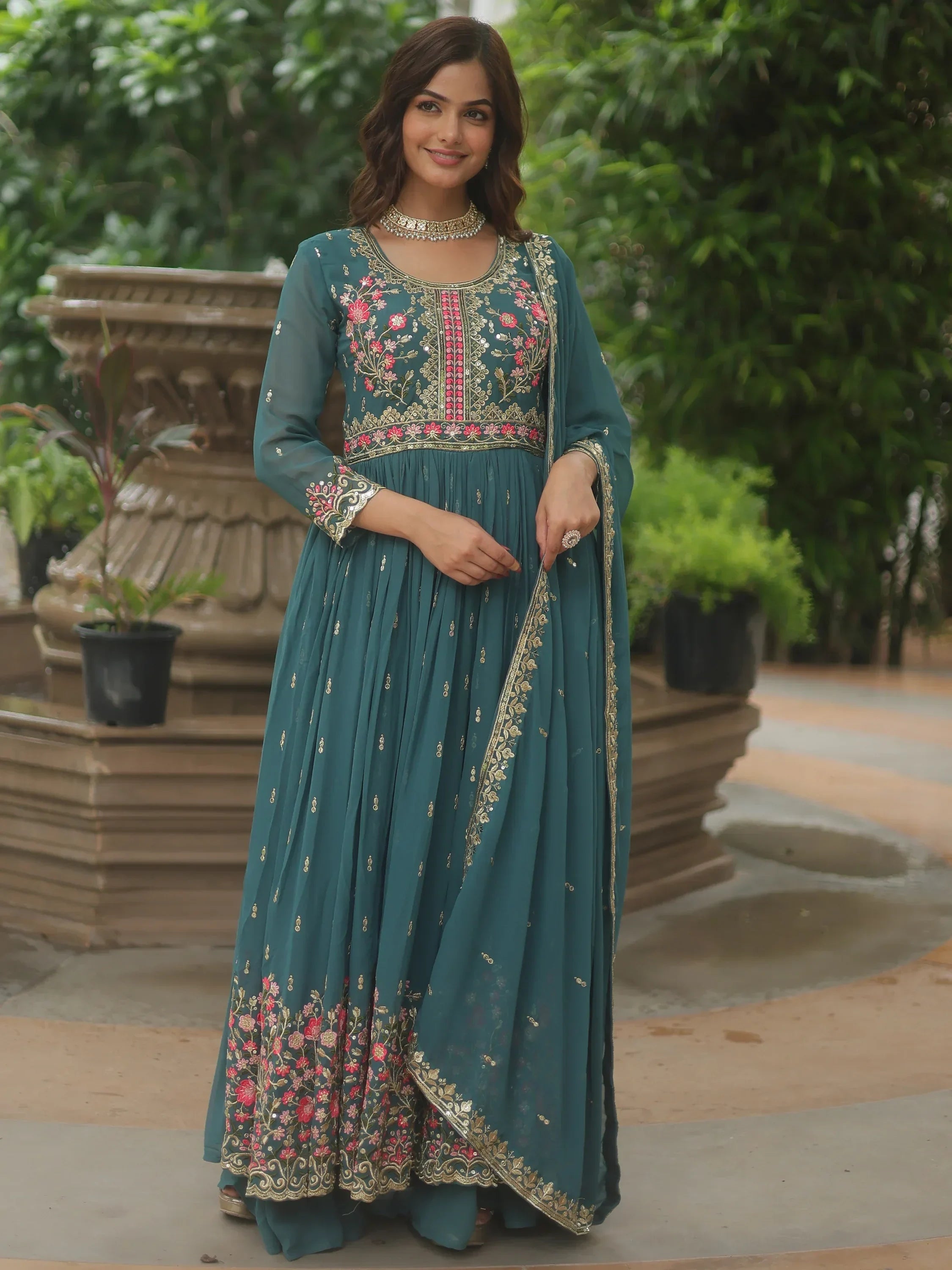 Woman wearing teal embroidered ethnic gown with floral detailing and dupatta outdoors