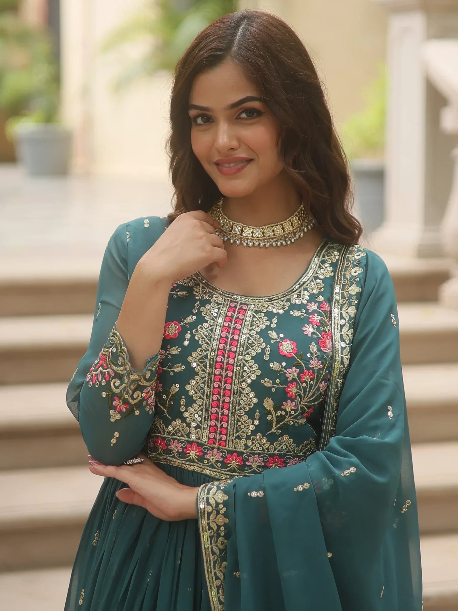 Woman wearing a teal embroidered Indian ethnic gown with gold and pink floral details
