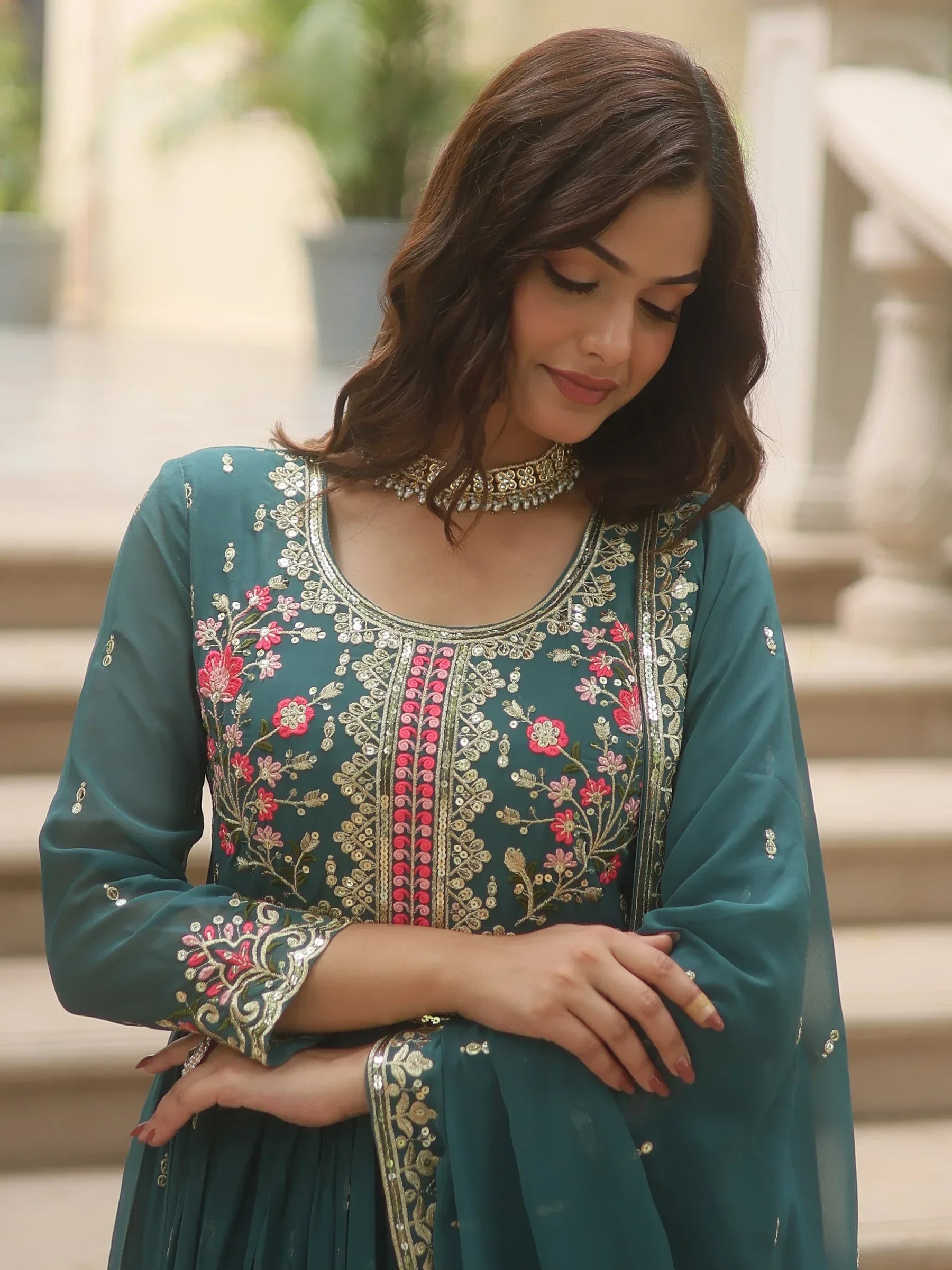 Woman in teal embroidered ethnic gown with floral patterns, posing outdoors
