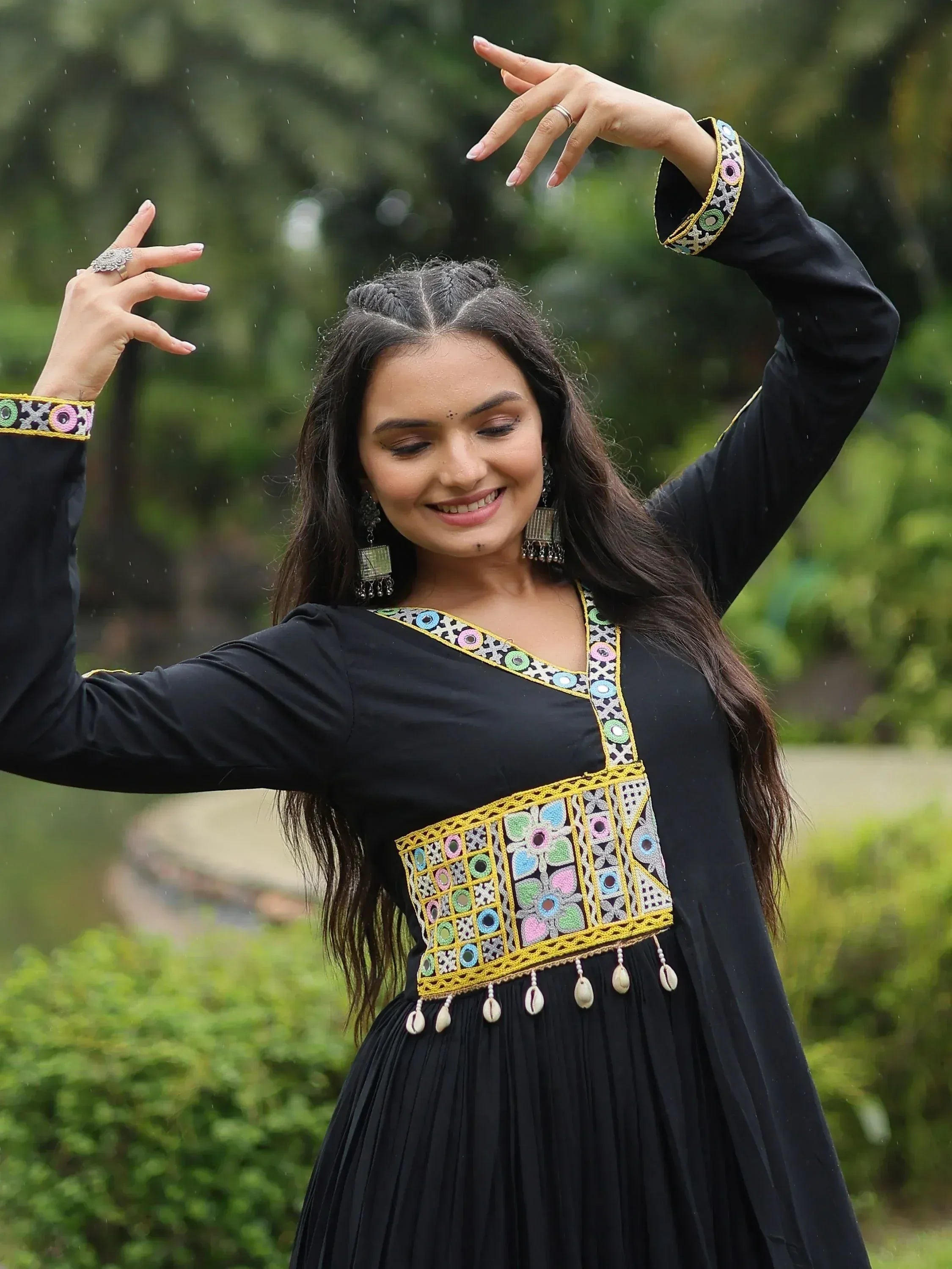 Woman in black ethnic gown with colorful mirror work and shell tassels, dancing outdoors