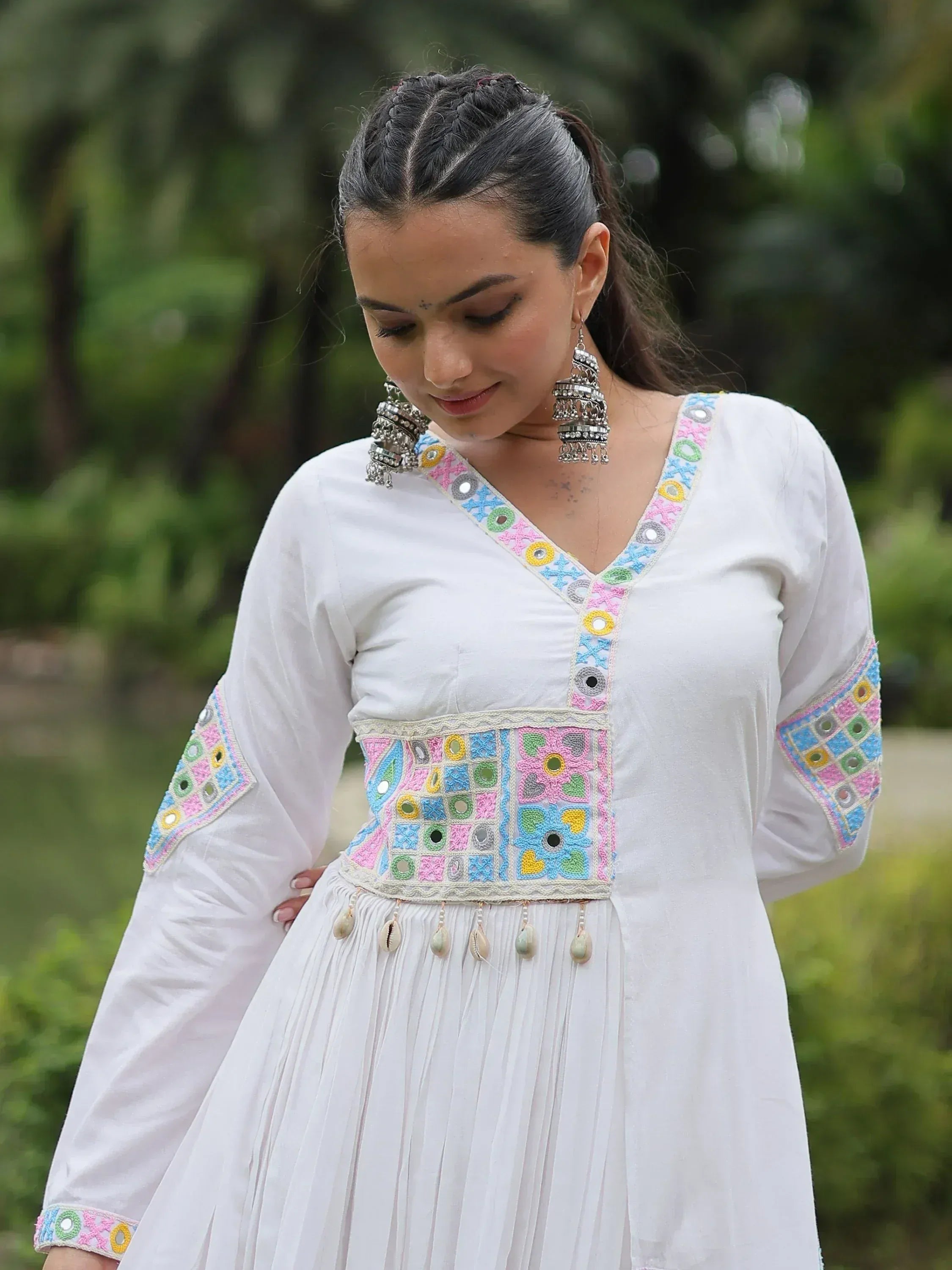 White ethnic gown with colorful mirror embroidery and shell tassels, perfect for Indian festive wear.