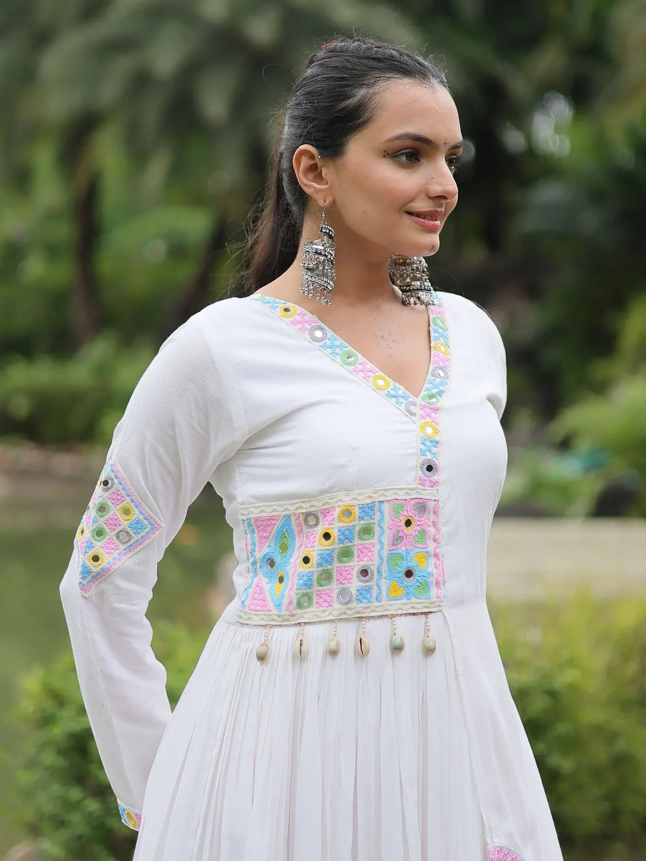 White ethnic gown with colorful mirror work and shell tassels, perfect for Indian occasions