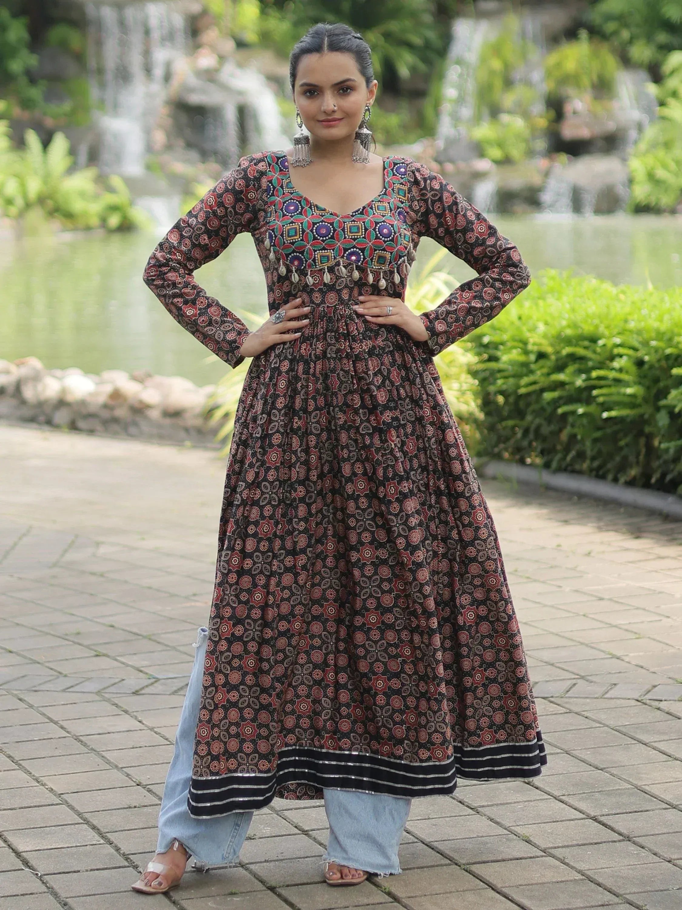 Woman in printed ethnic anarkali with mirror work, paired with jeans, standing outdoors near waterfall