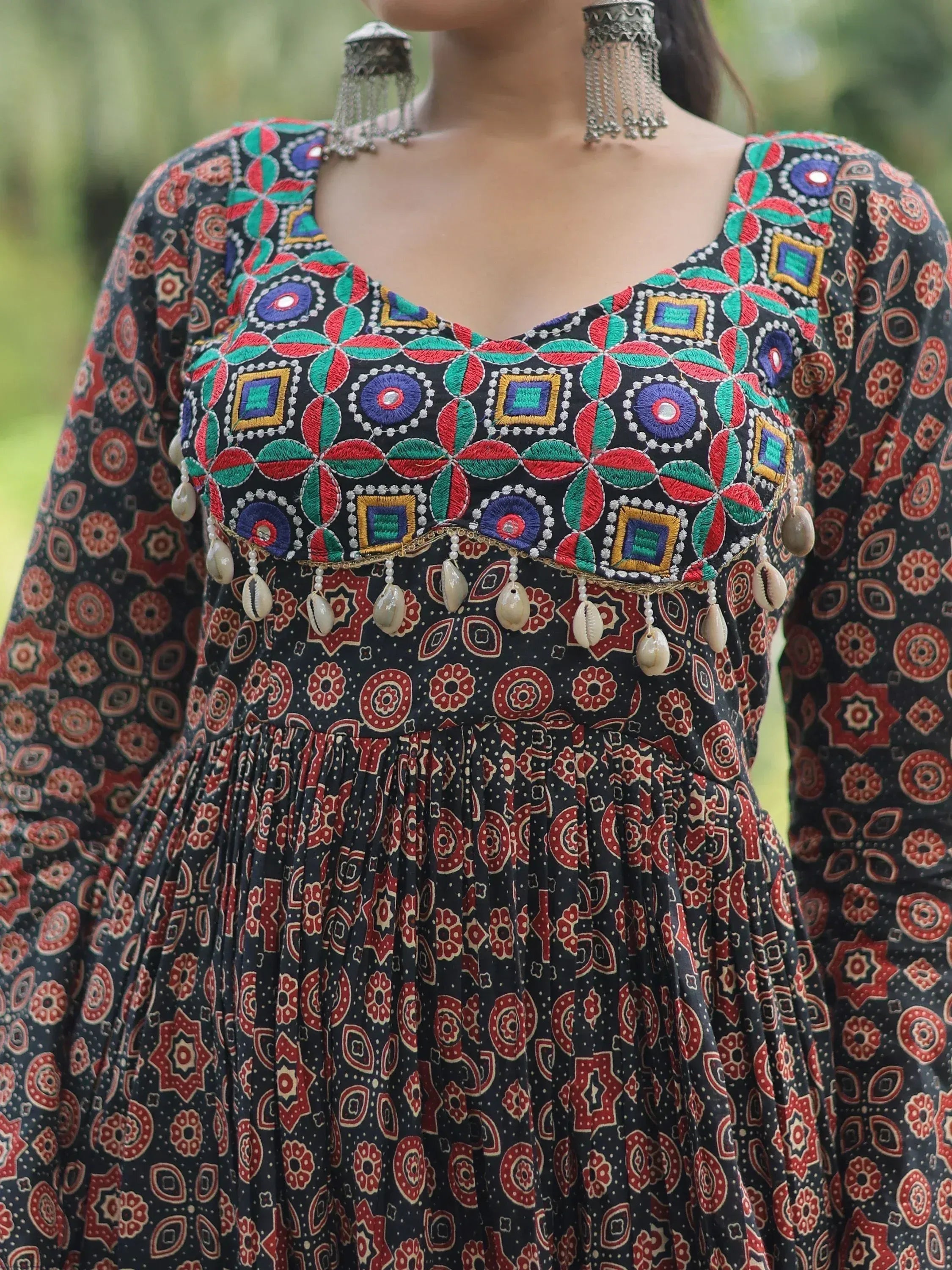 Black ethnic gown with colorful geometric embroidery, mirror work, and shell tassels, paired with silver jhumka earrings