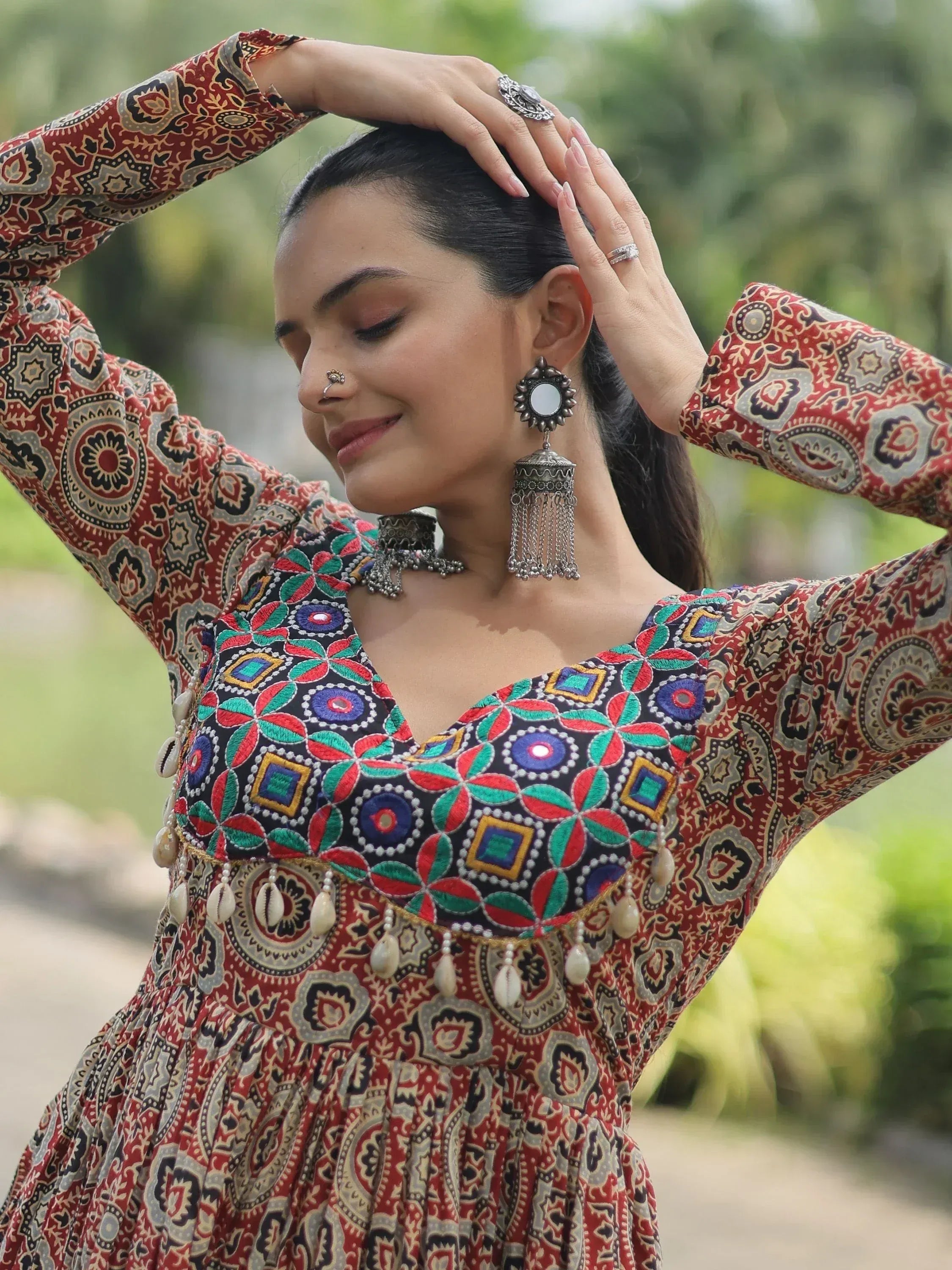 Woman in vibrant ethnic gown with mirror work, embroidery, and shell tassels, styled with traditional jewelry.