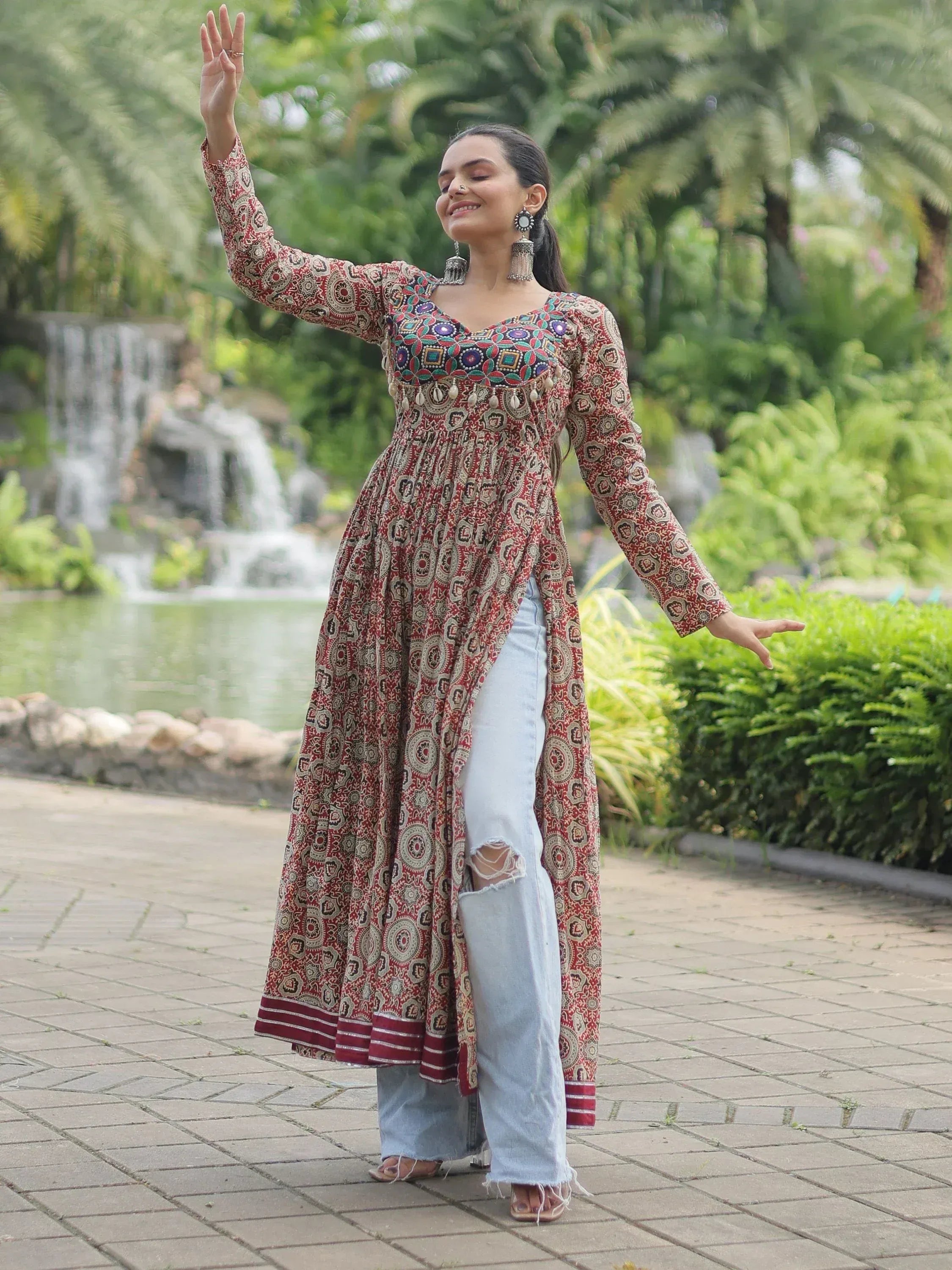 Woman in printed ethnic kurta with ripped jeans, dancing near garden waterfall