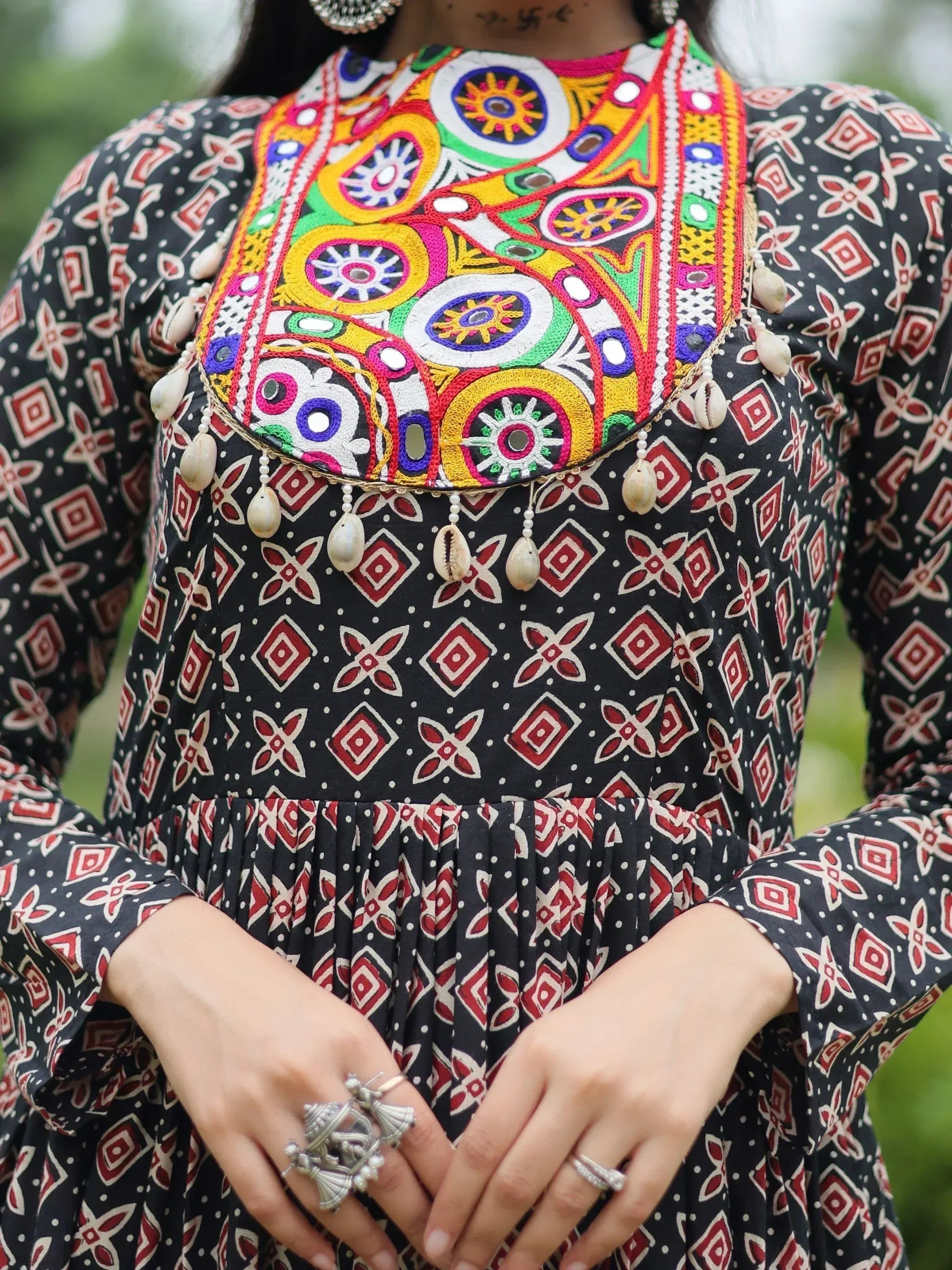 Black ethnic dress with colorful mirror embroidery, shell tassels, and geometric print, paired with silver jewelry
