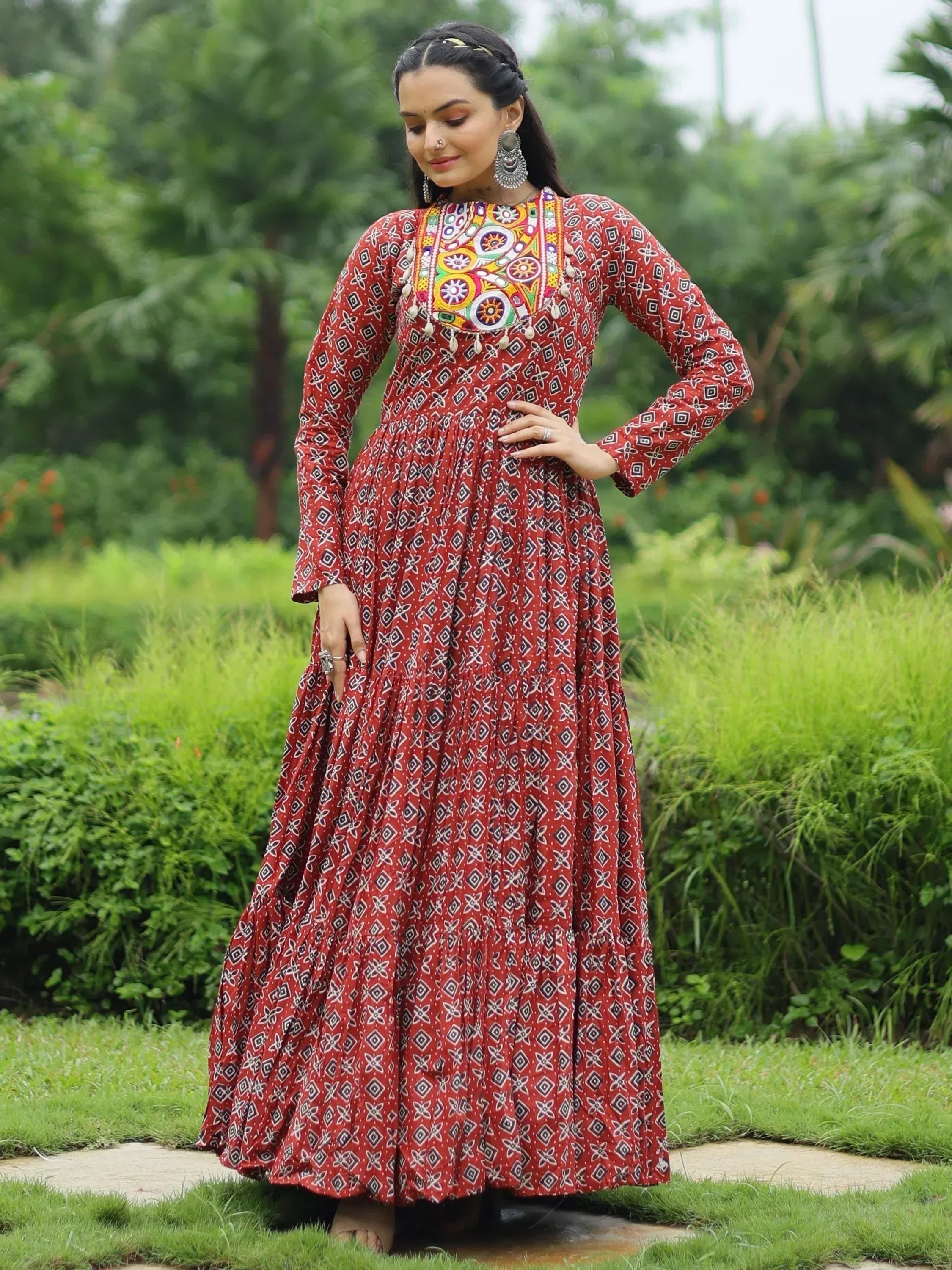 Woman in red printed ethnic gown with colorful embroidery, standing in garden
