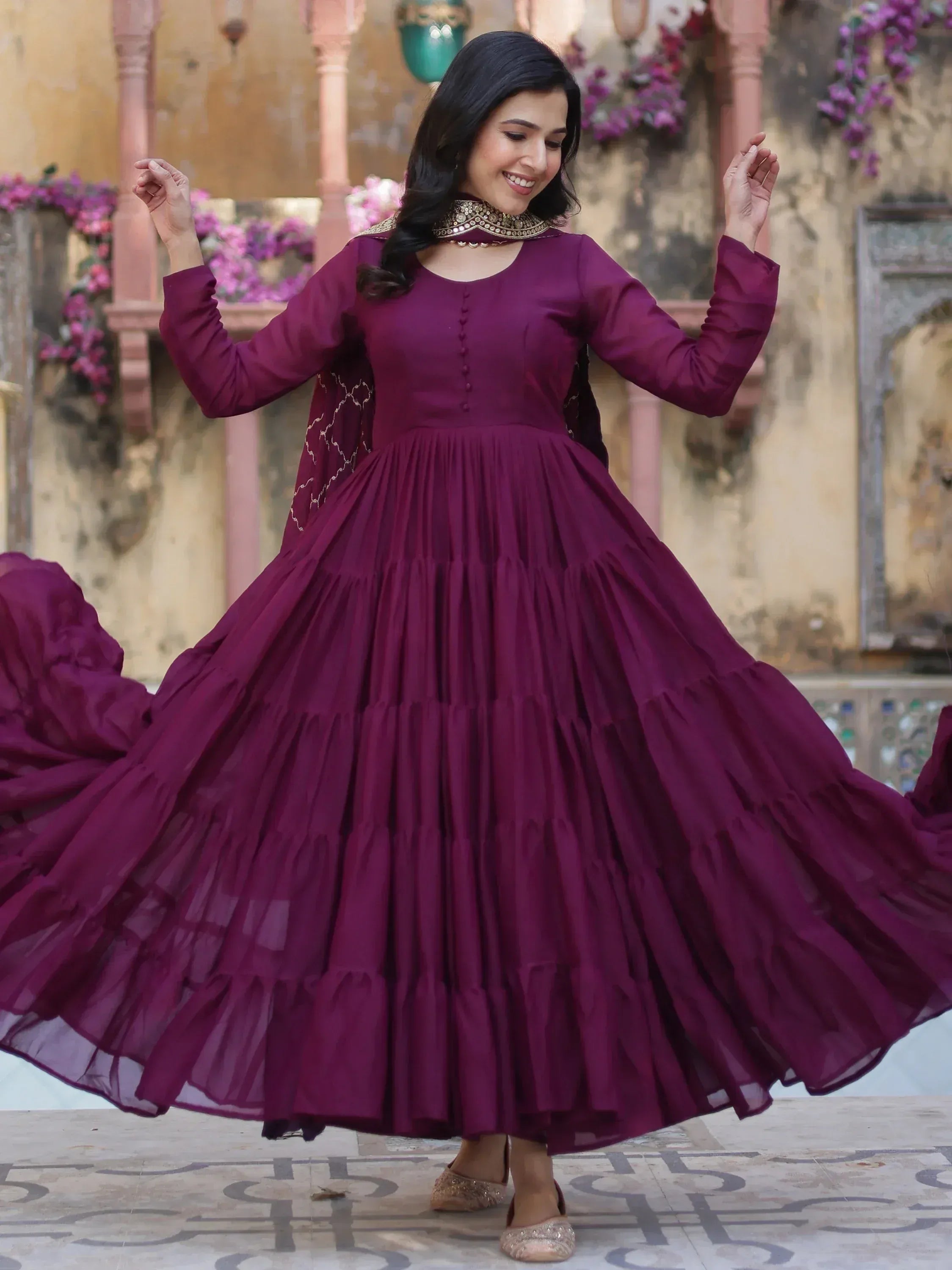 Woman twirling in a maroon ethnic gown with layered skirt and gold embroidery, perfect for festive occasions.